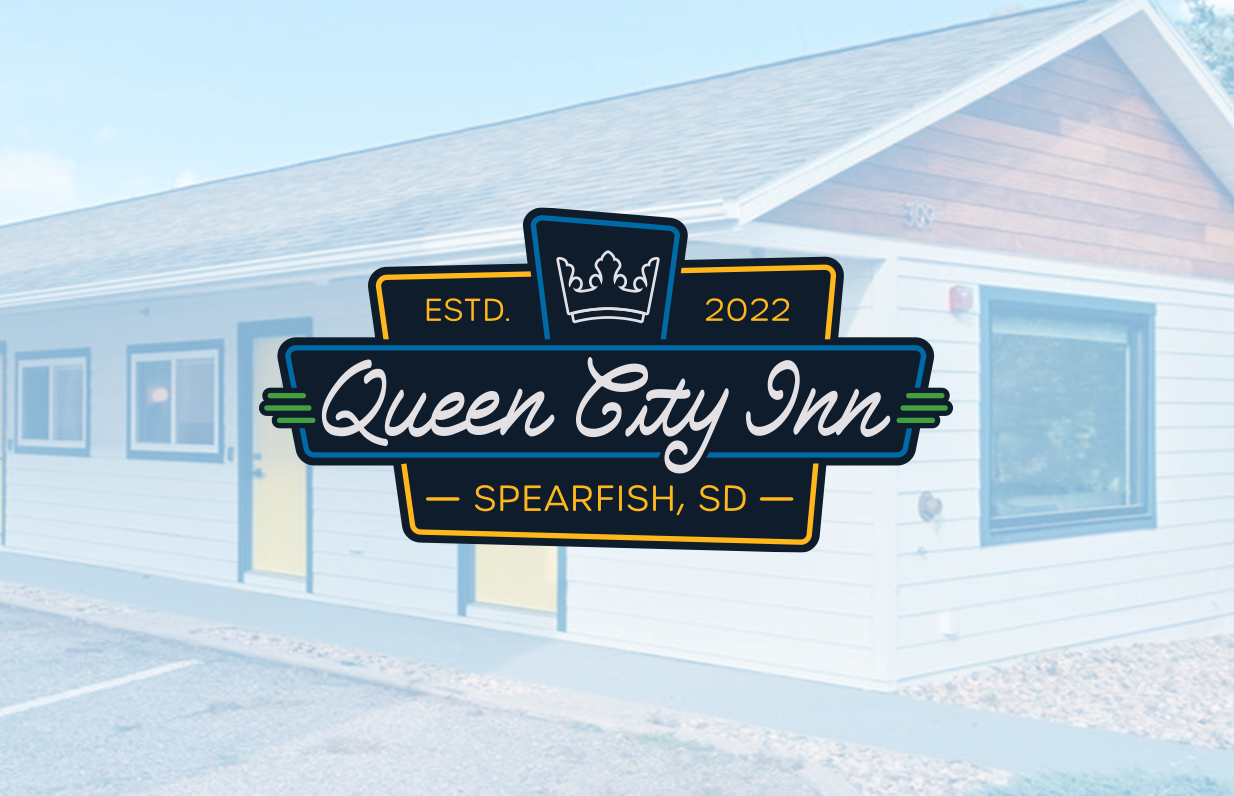 Logo for Queen City Inn over a faded background of a white building with a gabled roof, windows, and a door, situated in Spearfish, South Dakota.