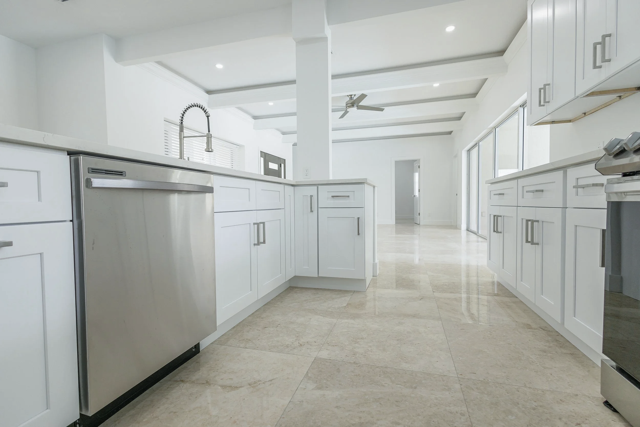 Modern white kitchen with granite countertops, stainless steel appliances, and large windows letting in natural light.