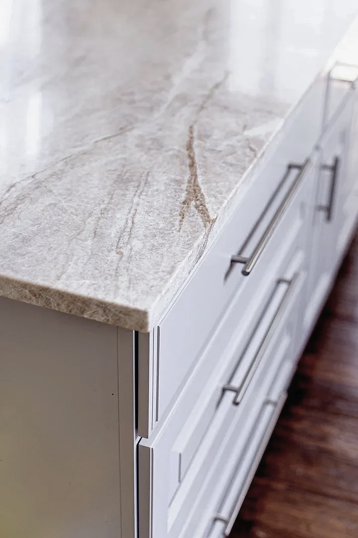 Close-up of a kitchen countertop with light-colored marble surface and white cabinets with metal handles.