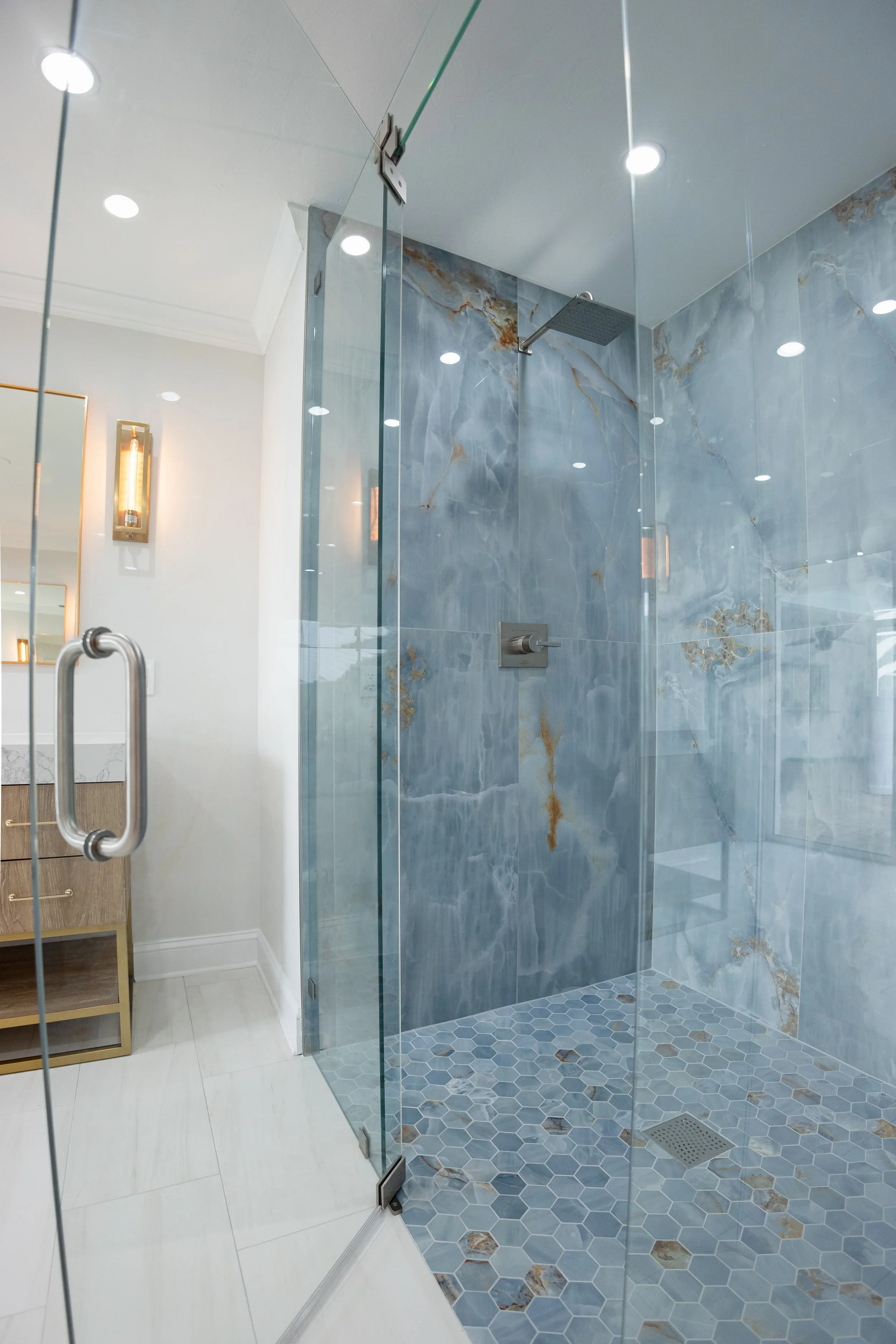 Modern glass shower with blue marble tiles and hexagonal stone tiles on the floor, with a rain showerhead and a control handle inside.