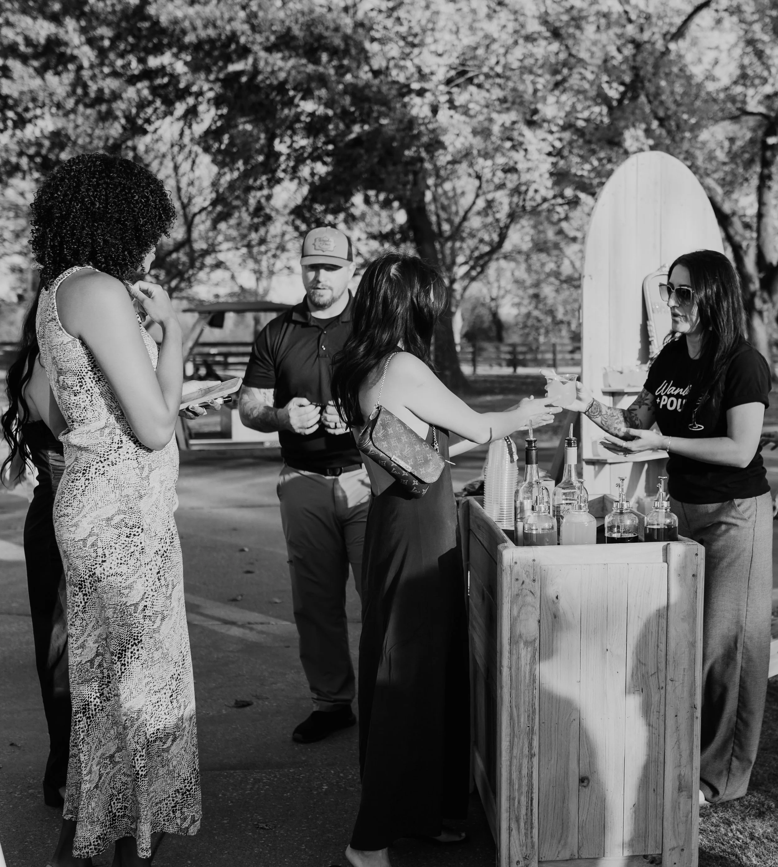 Outdoor cocktail wall and cart setup by Wander + Pour with guests enjoying cocktail hour at a wedding or event in Oklahoma.