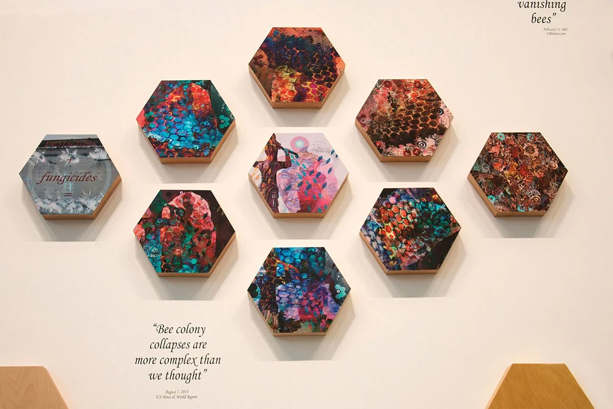 A display of ten hexagonal artwork pieces arranged in a pattern on a wall, with vibrant abstract designs resembling bees and honeycomb patterns, and a quote about bee colony collapses.