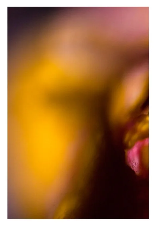 Blurred close-up of a person smiling or laughing, with pink, yellow, and dark tones.