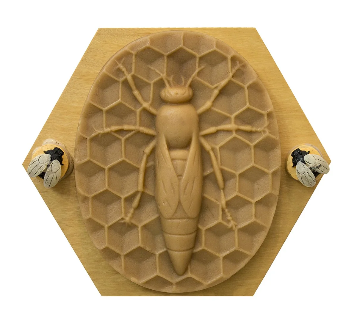 3D soap sculpture of a bee, placed on a honeycomb-patterned oval base with two smaller bee sculptures on each side on a wooden platform.