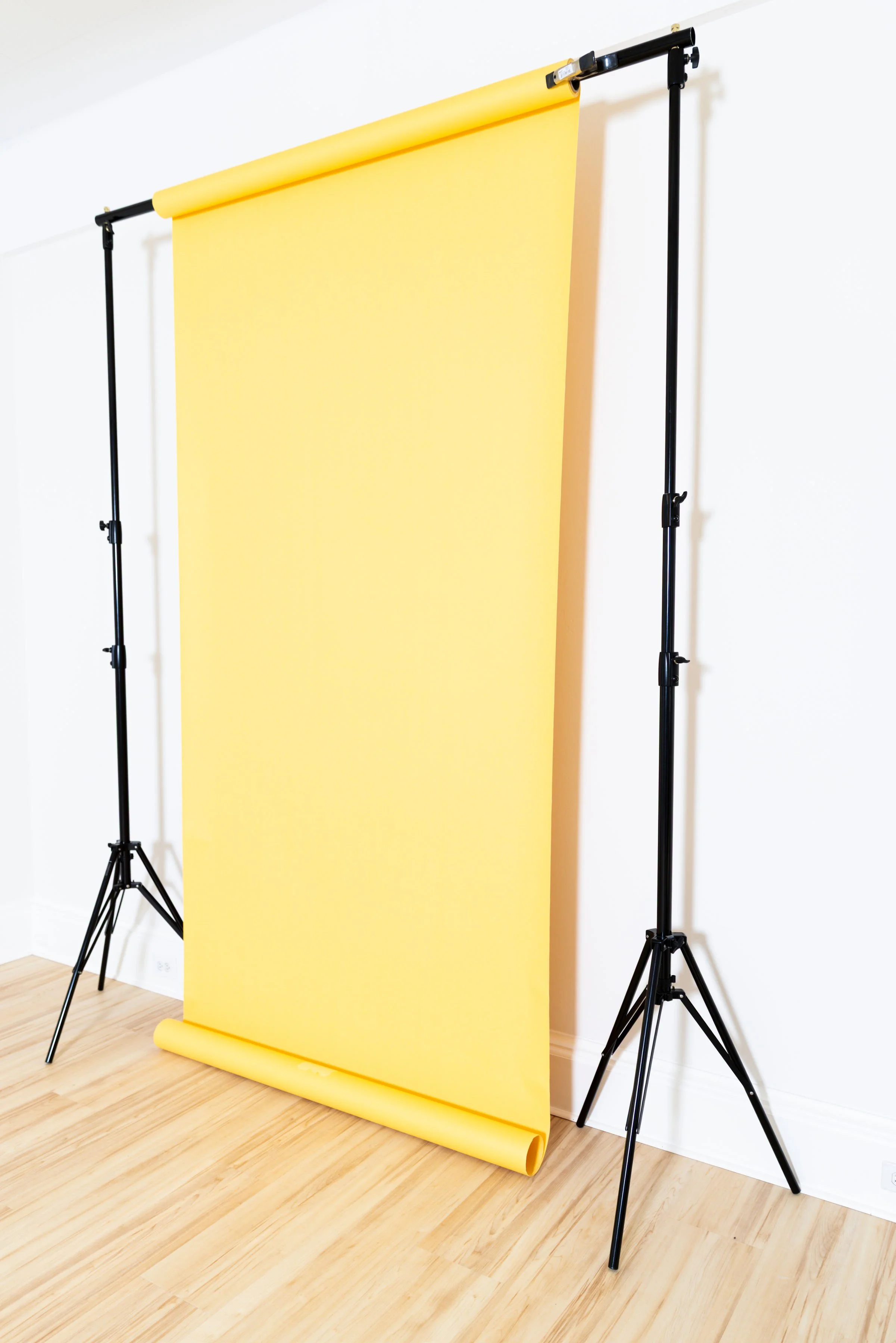A yellow backdrop stand with a roll of yellow paper on a wooden floor, set up in a white room.