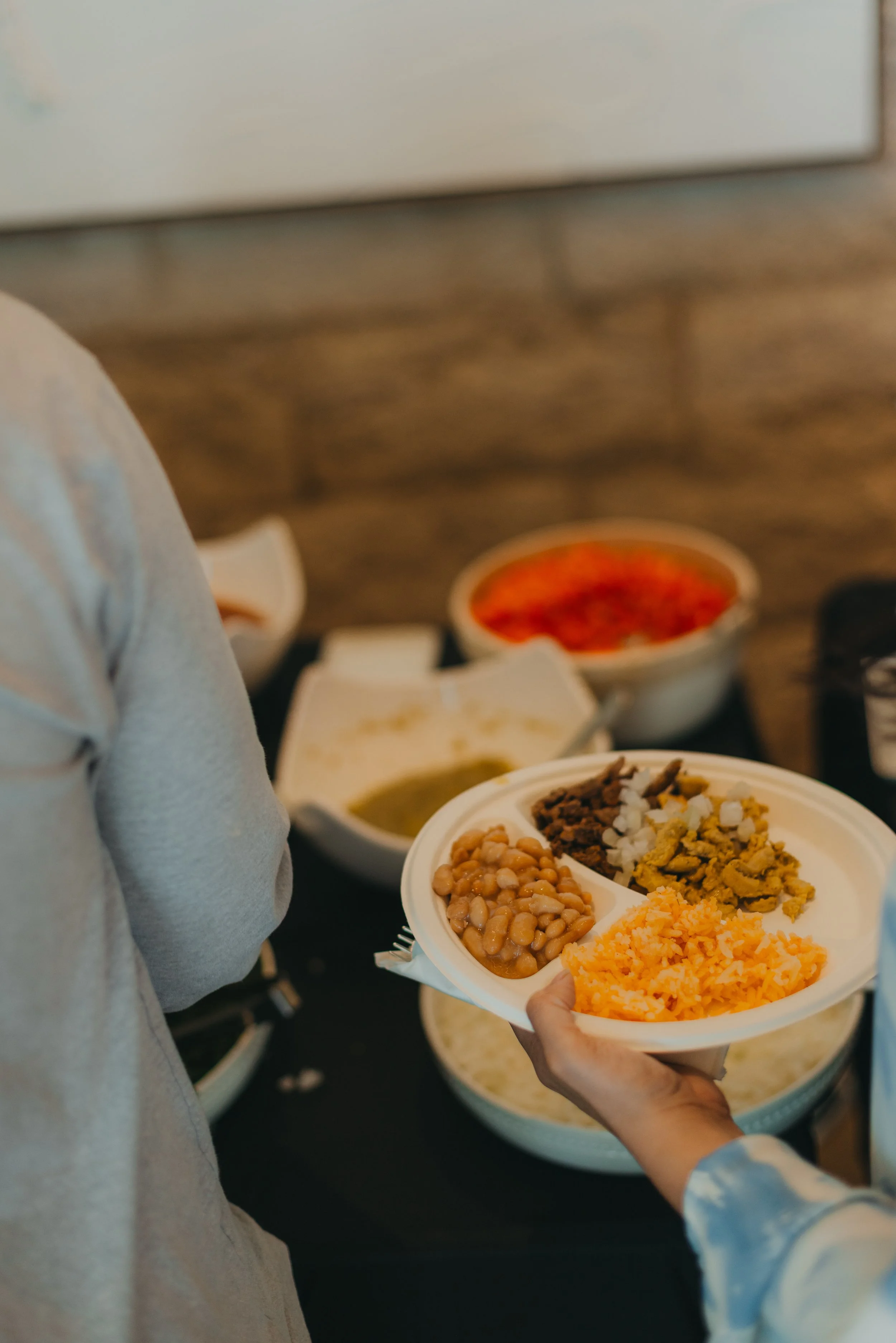 Person serving food from a plate with beans, rice, and other dishes at a buffet table.