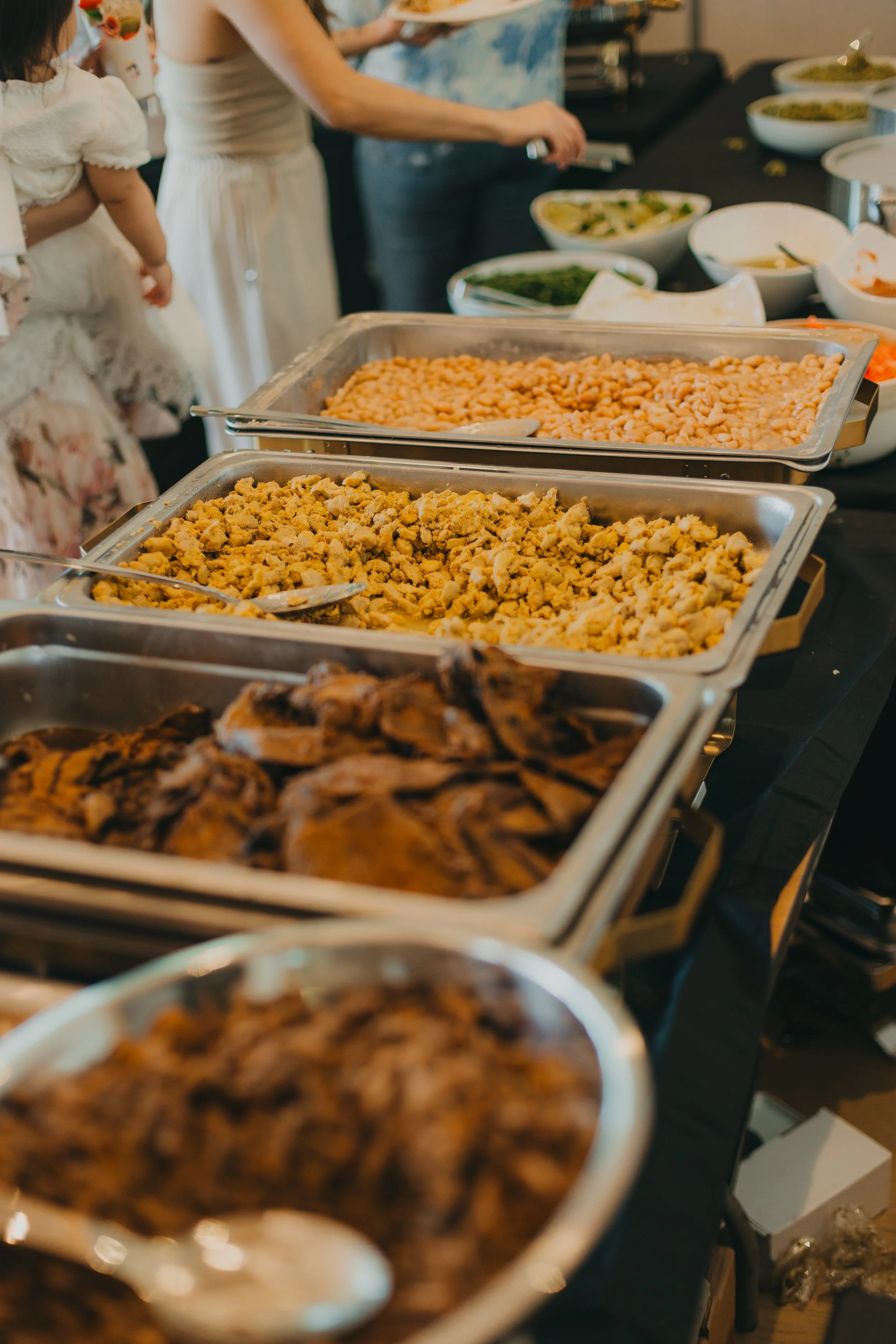 Buffet table with trays of scrambled eggs, roasted chicken, and other dishes, with bowls of condiments and salads in the background.