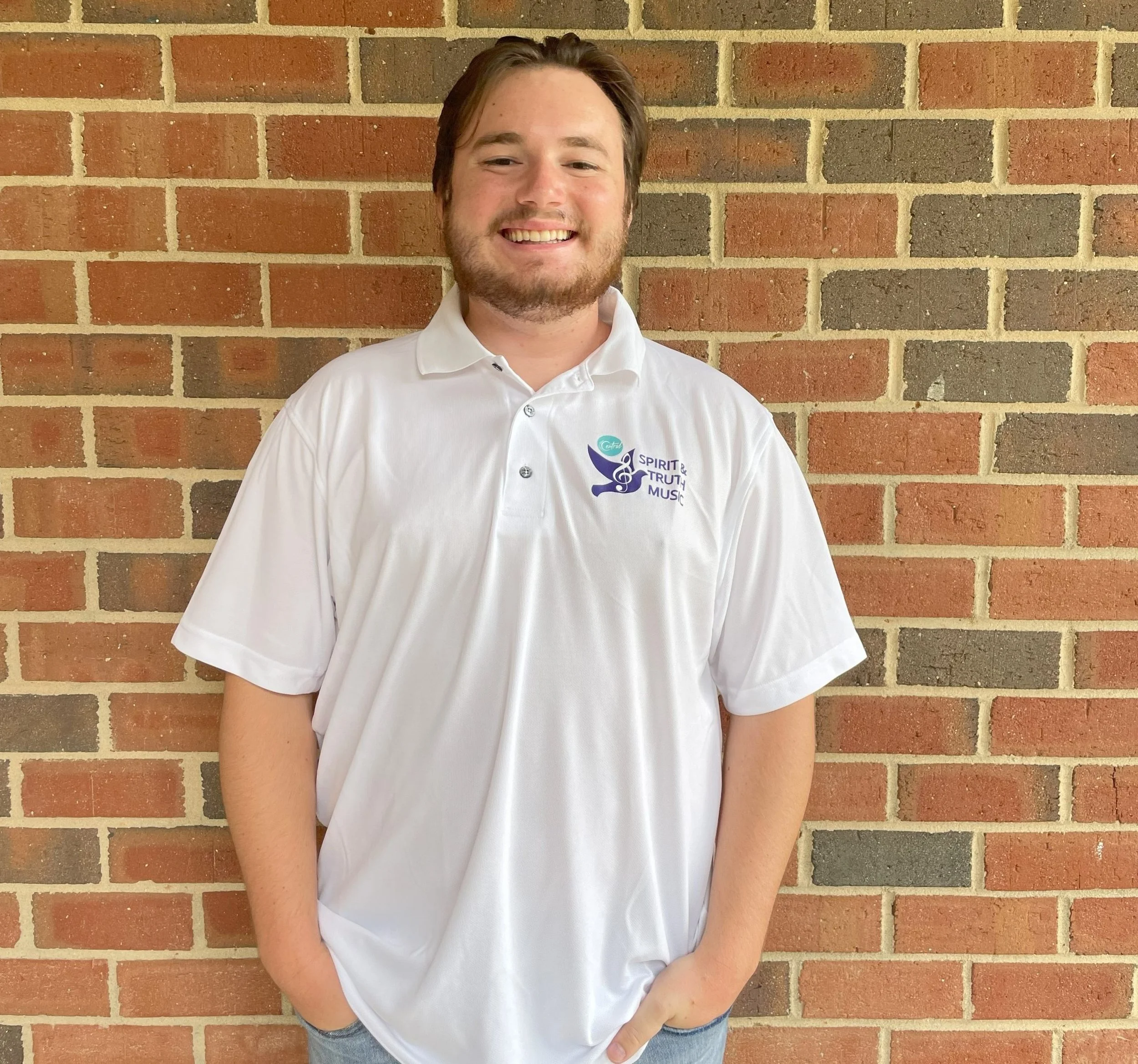 man with white polo standing against brick wall