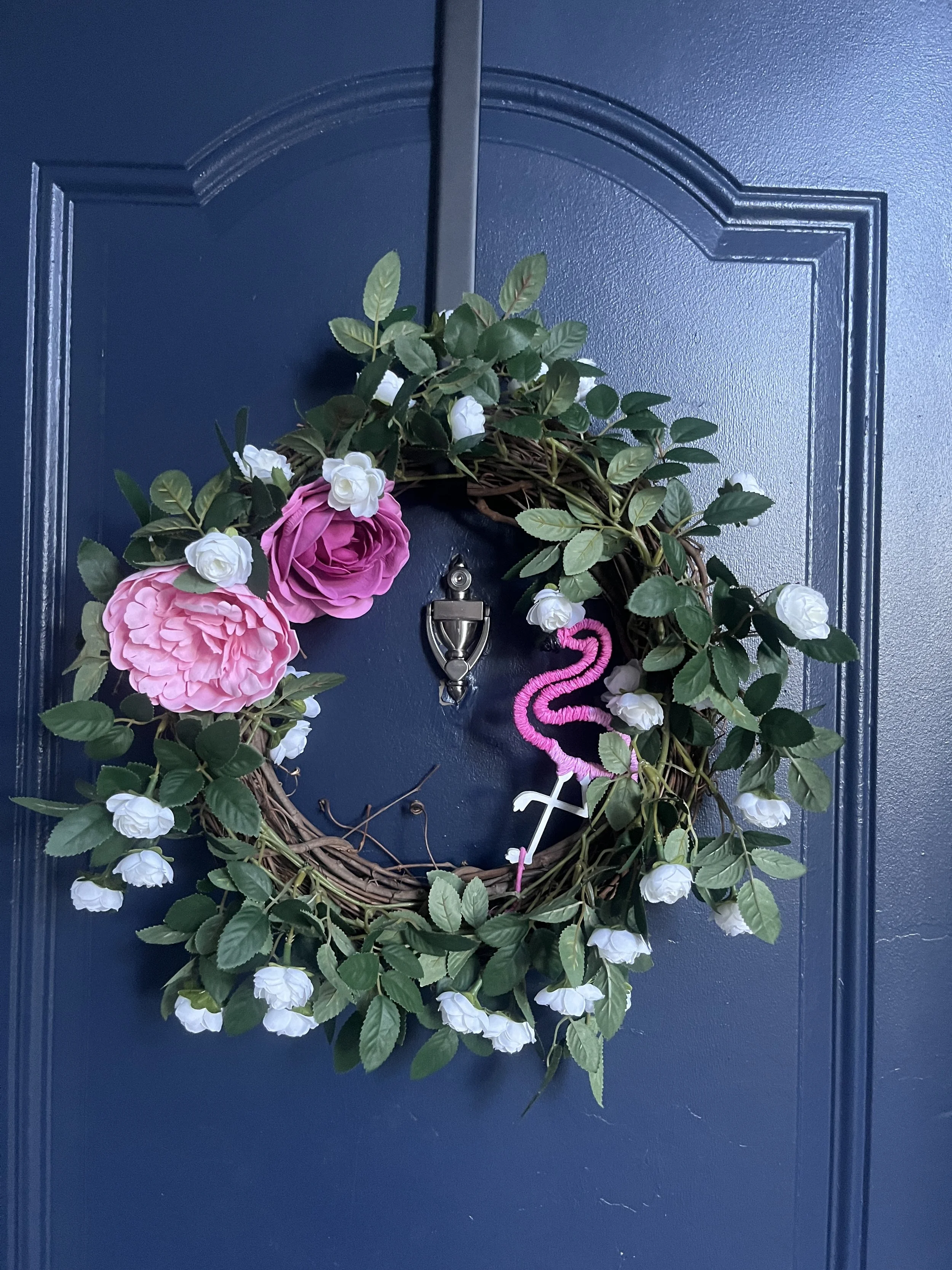 A decorative flower wreath with pink and white flowers hanging on a blue door.