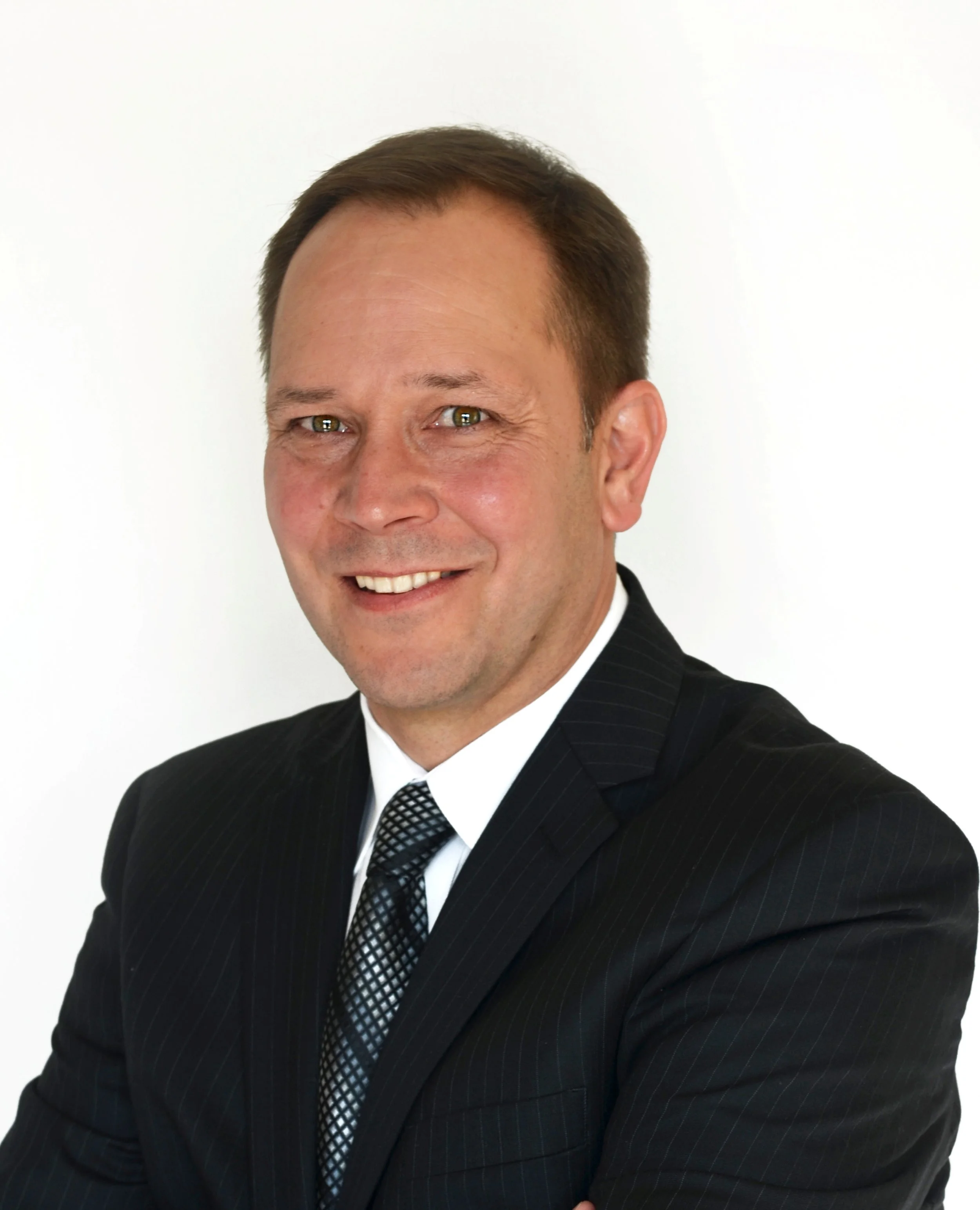 Professional man in a black pinstripe suit, white shirt, and patterned tie smiling against a plain white background.