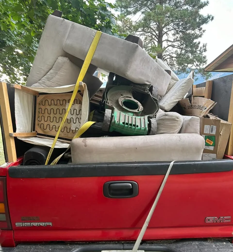 Red GMC Sierra pickup truck loaded with furniture and household items, including a mattress, chair, sofa, and cardboard boxes.