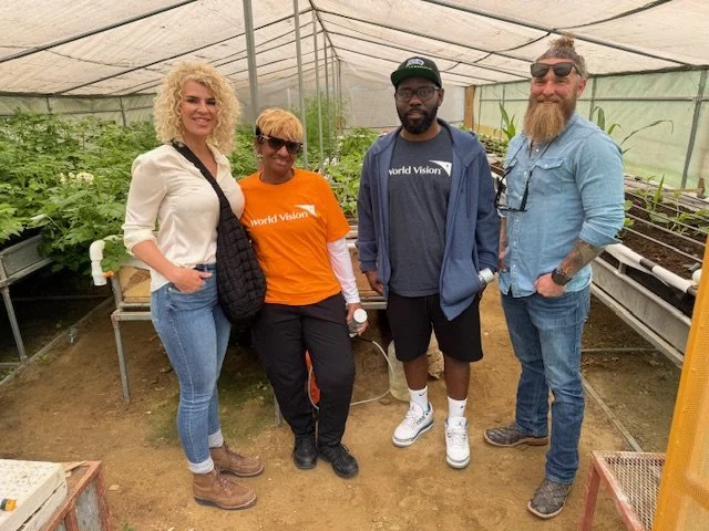 Four people standing inside a greenhouse with plants, smiling for the photo.