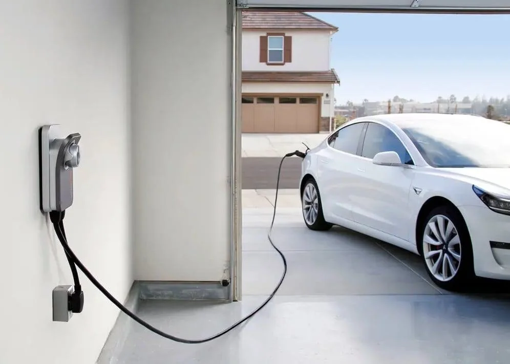 Electric car charging in a garage with a white Tesla connected to a charging station.