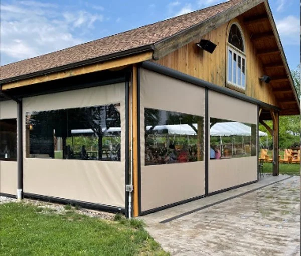 A building with a wooden upper section and beige enclosed patio area with large windows under a blue sky with some clouds.