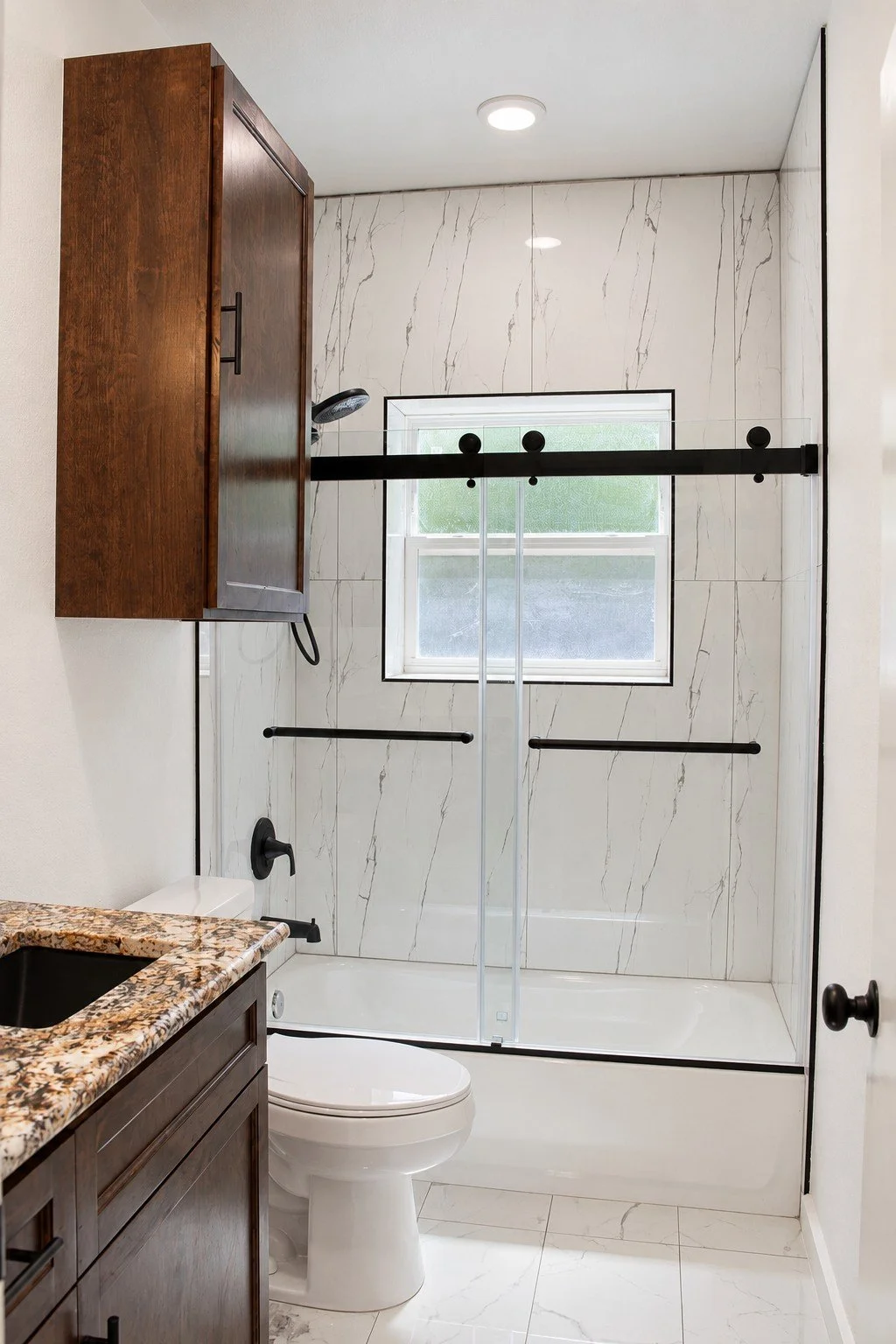 Secondary bathroom with a stain-grade wood vanity, granite countertop, black fixtures, and a glass-enclosed tub and shower.