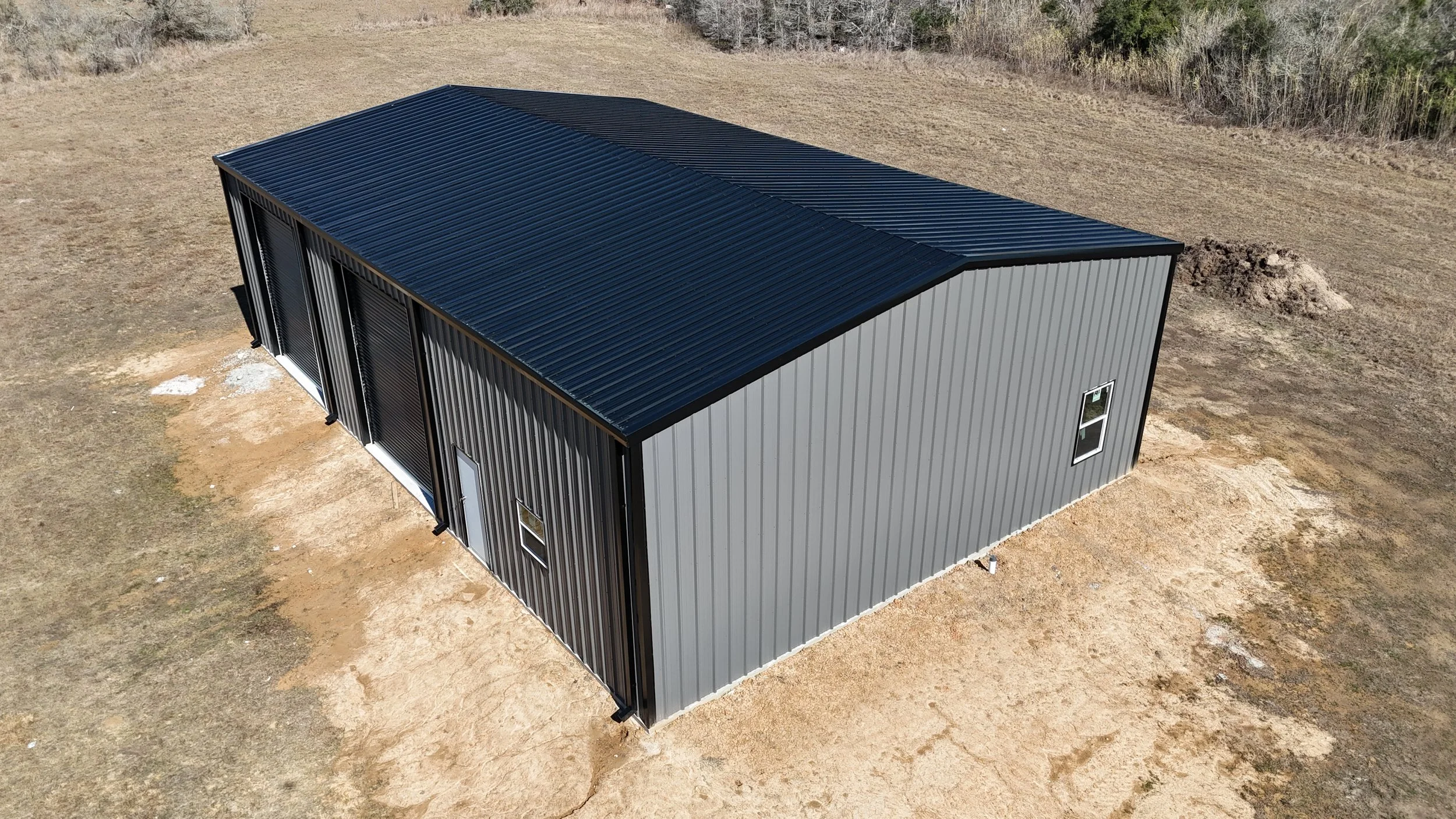 Drone view of a fully insulated custom metal shop in Wallis, TX with black roof and roll-up doors, built for long-term performance.