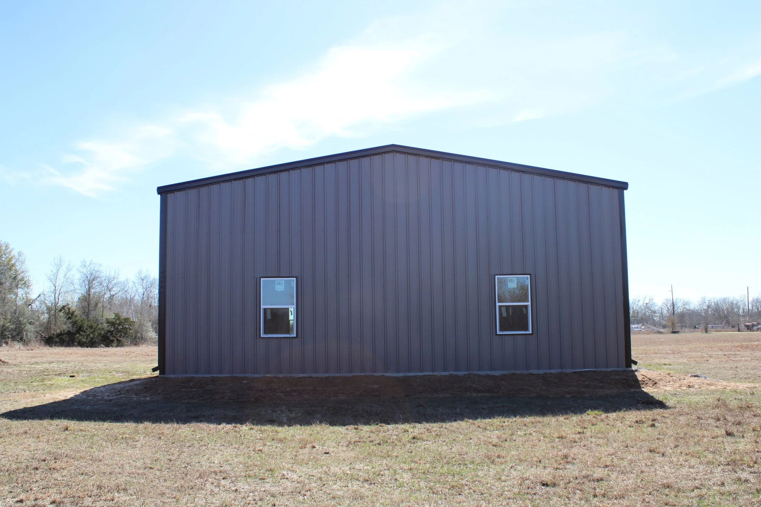 Side view of a fully insulated custom metal shop in Wallis, TX showing residential windows and durable metal siding built for Texas conditions.