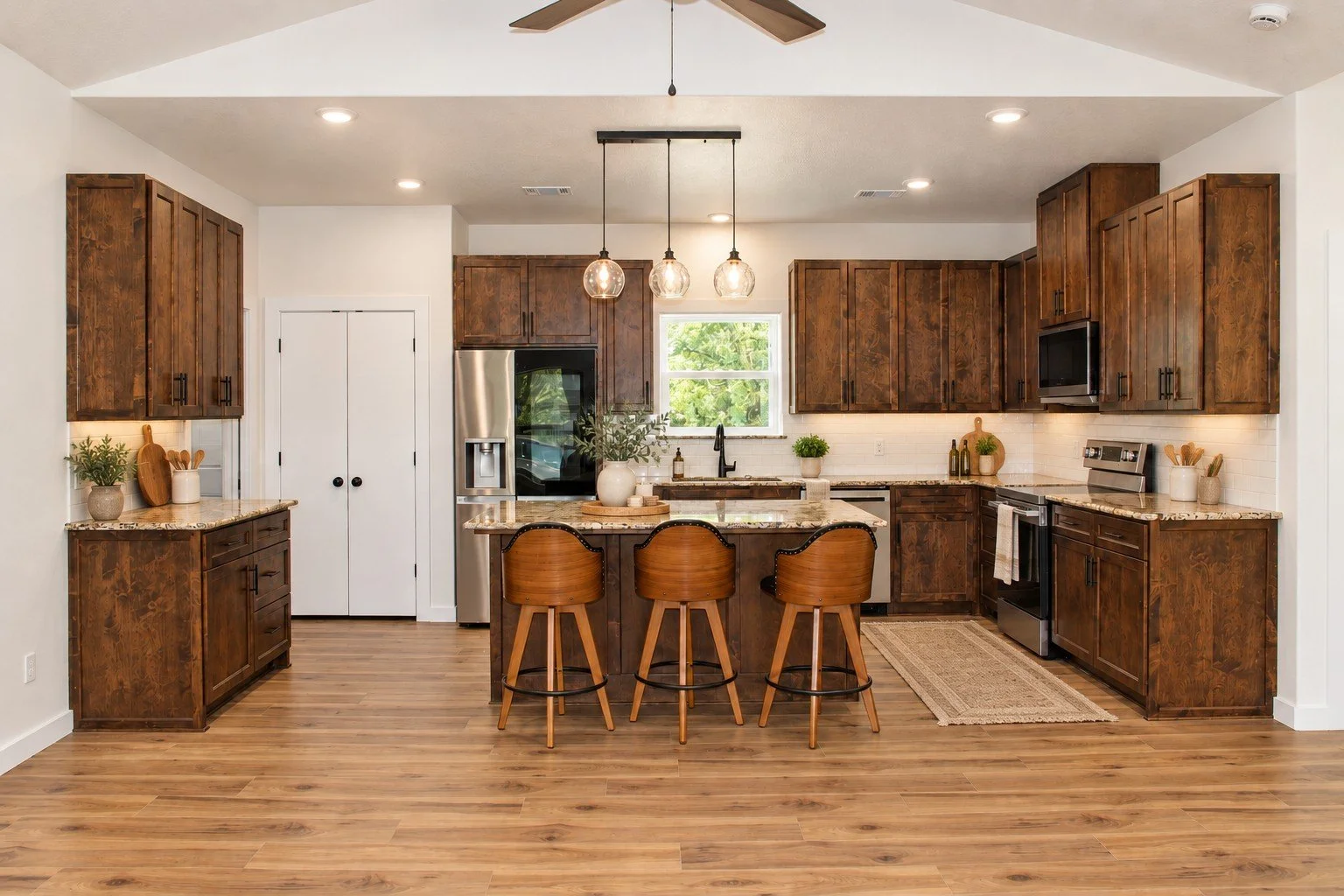 Custom barndominium kitchen featuring stain-grade wood cabinets, granite countertops, a large center island, stainless-steel appliances, and wood-look tile flooring.
