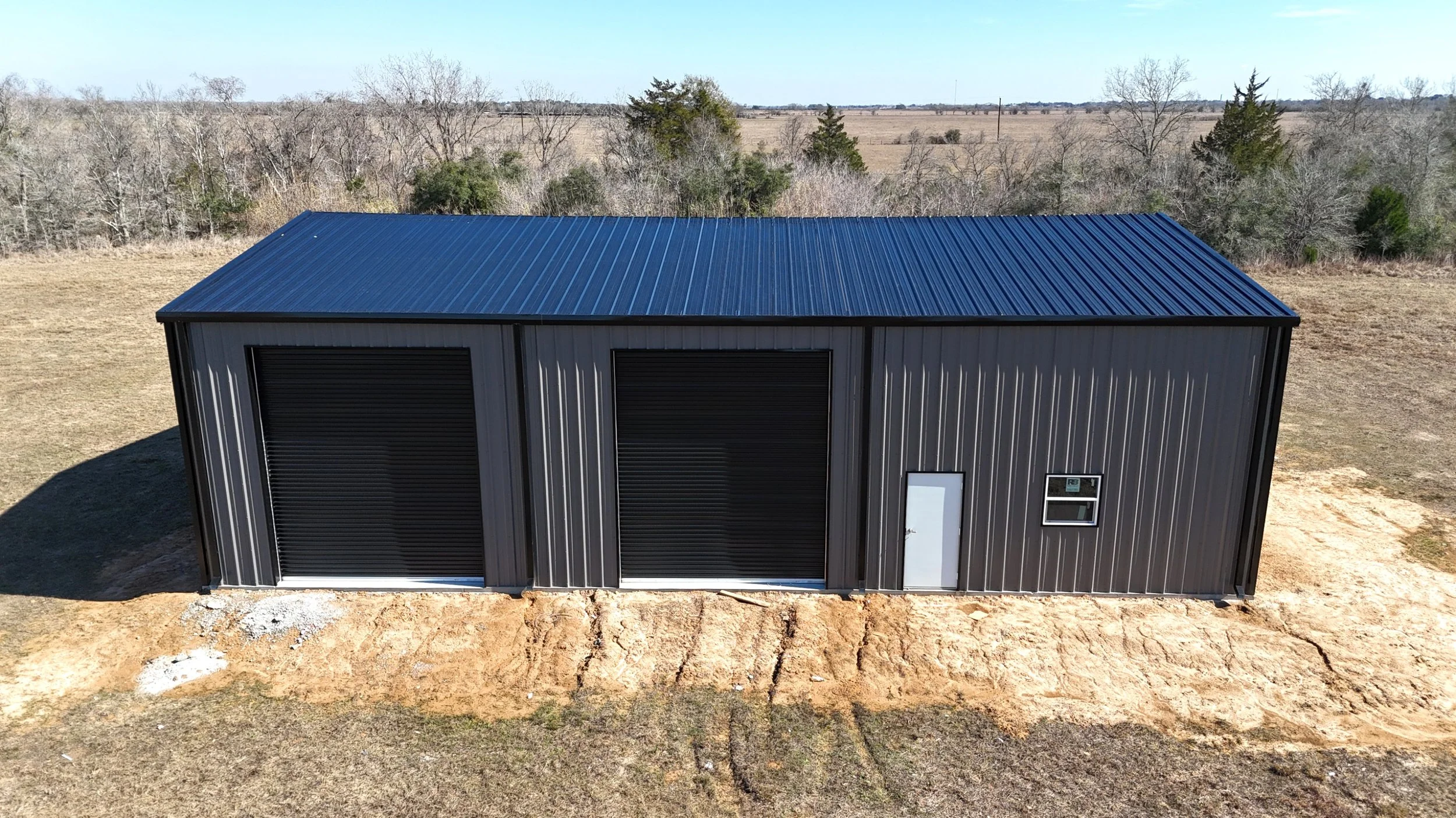 Custom 60’ x 40’ fully insulated metal shop in Wallis, TX featuring three black insulated roll-up doors, 16’ eave height, and a clean modern design built for Texas durability.