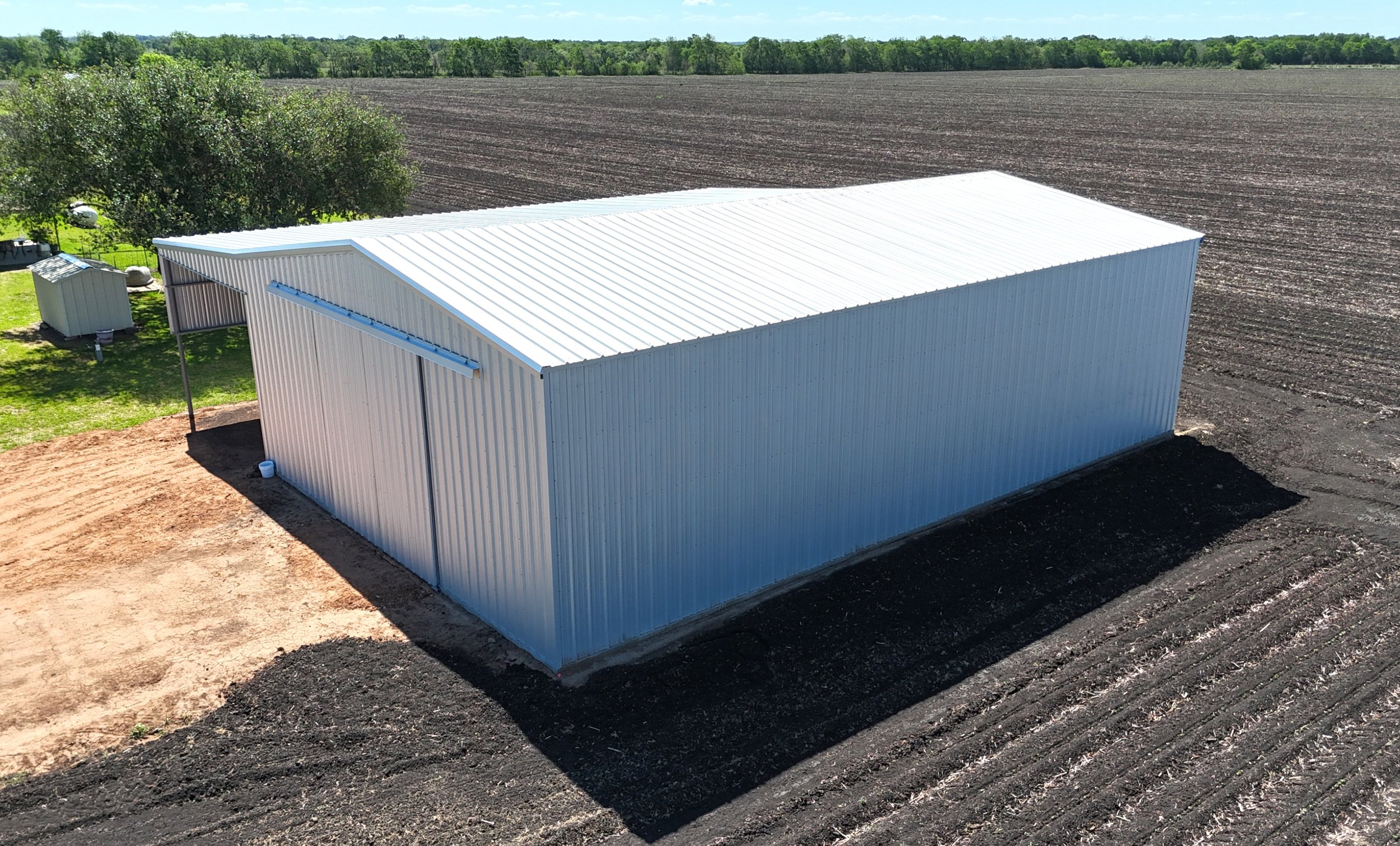 Side view of agricultural metal shop with lean-to and equipment storage, galvalume panels, East Bernard TX