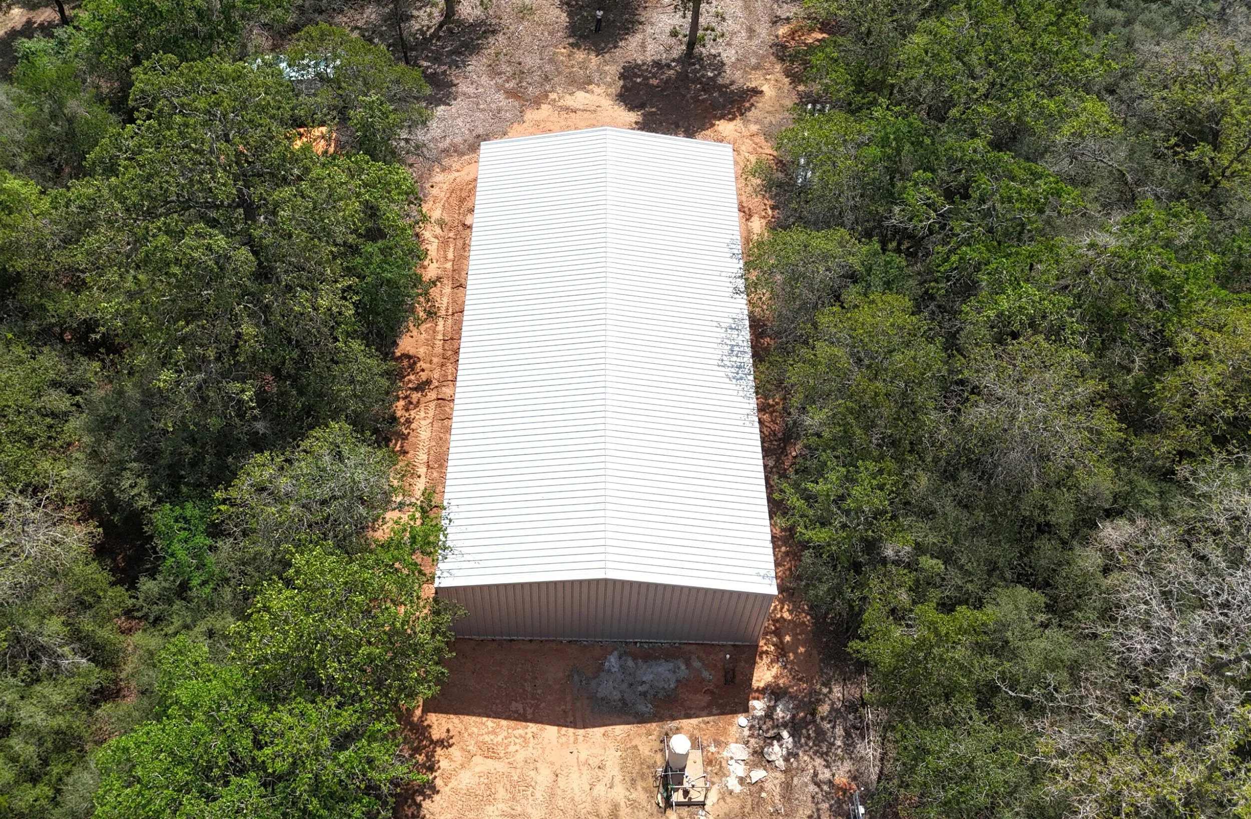 Aerial view of custom 40x60x14 metal shop with full front awning and Galvalume roof in Waelder, TX surrounded by trees