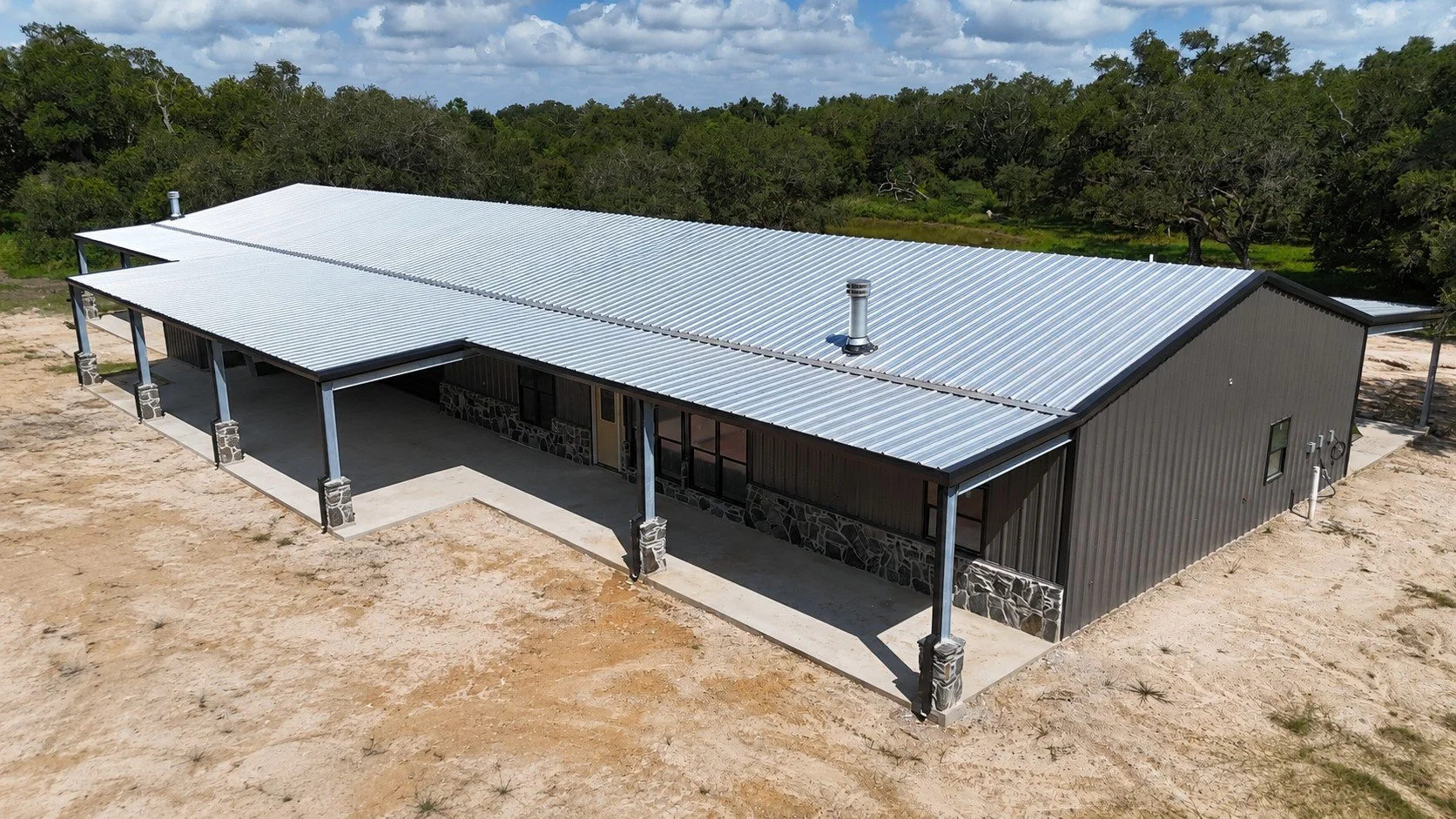 Aerial view highlighting the barndominium’s Galvalume roof, covered front porch, Charcoal Gray exterior, and stone-accented columns.