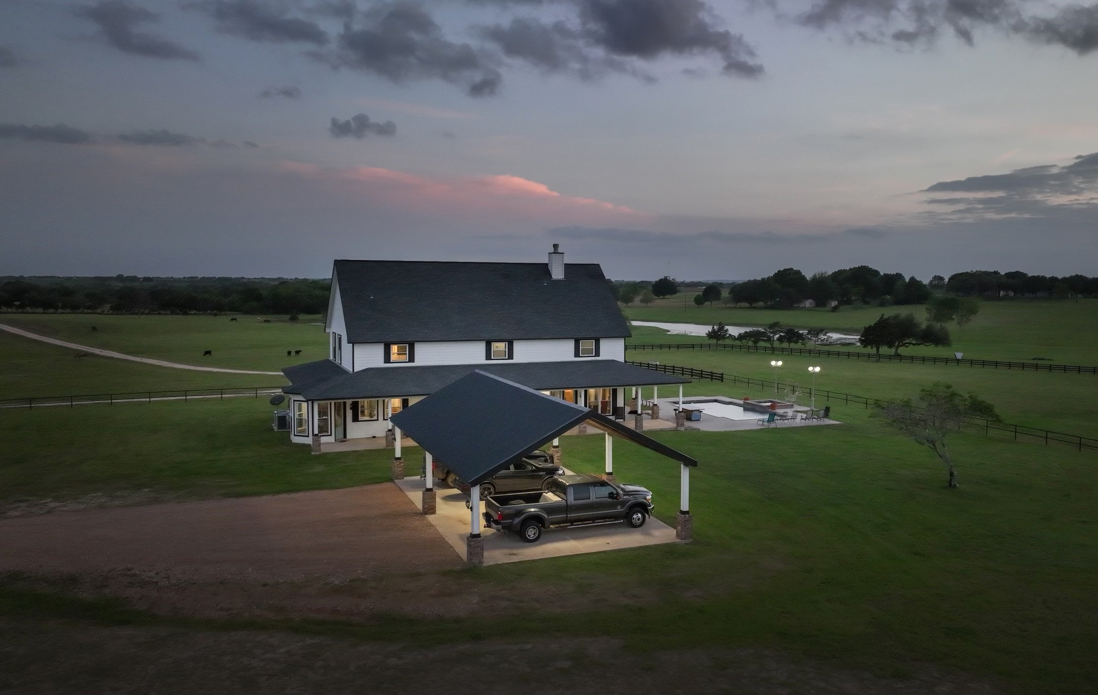 This custom-built home sits on a beautiful acreage in New Ulm, Texas, complete with a wrap-around porch, attached carport, pool, hot tub, and sweeping countryside views.