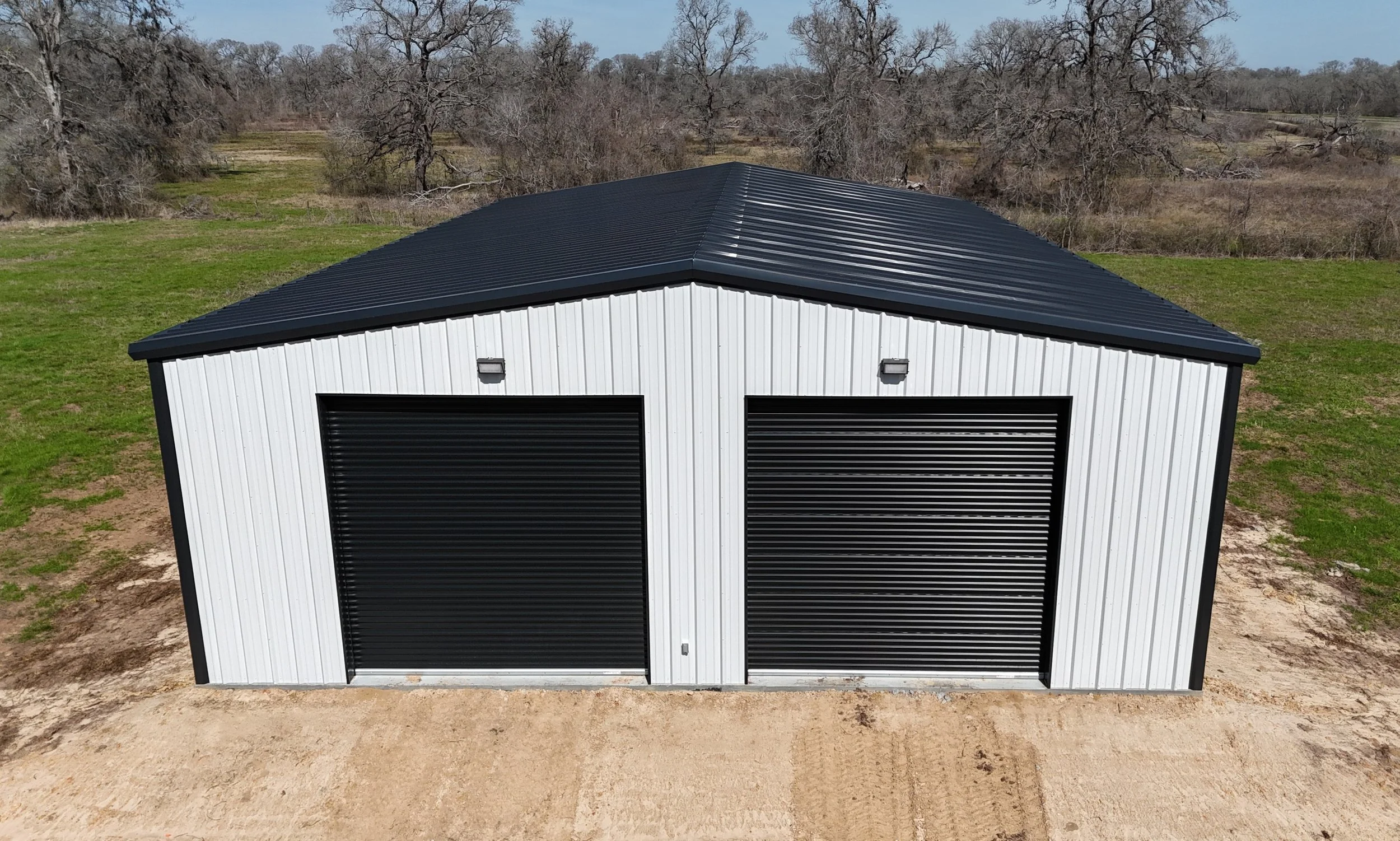 40’ x 60’ x 16’ custom metal building in Fulshear, TX featuring a classic white exterior with black trim, black roof, and two 14’ x 14’ roll-up doors for equipment and recreational vehicle storage.