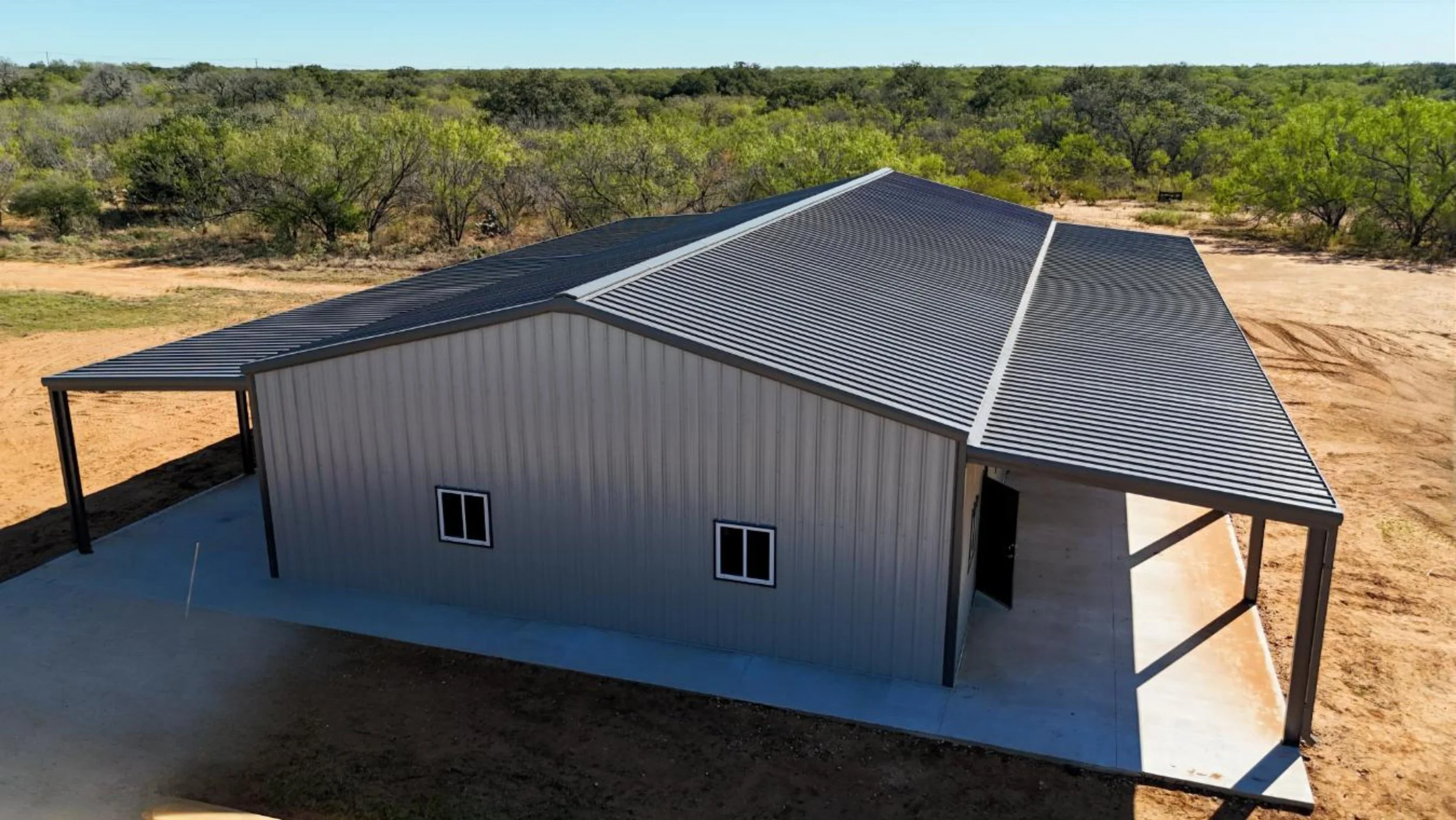 Large Mueller metal barndominium in Bigfoot Texas with charcoal roof and dual lean-to covered porches on concrete slab.