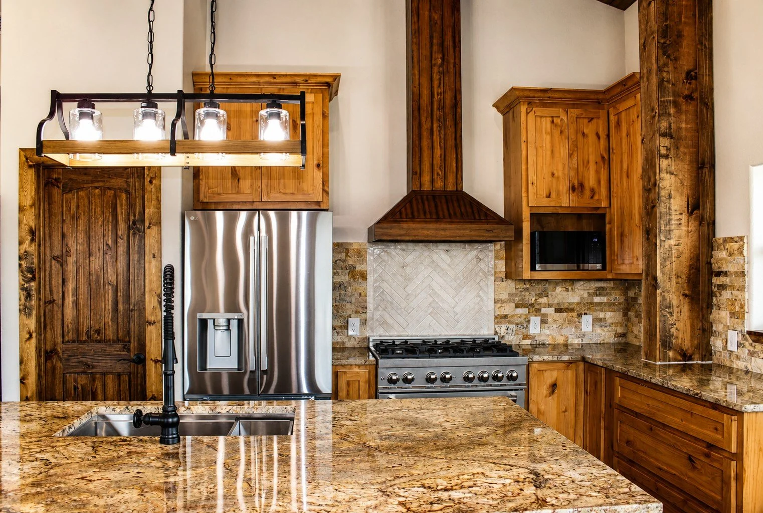 Custom farmhouse kitchen featuring granite countertops, wood cabinetry, and stainless appliances inside Texas barndominium
