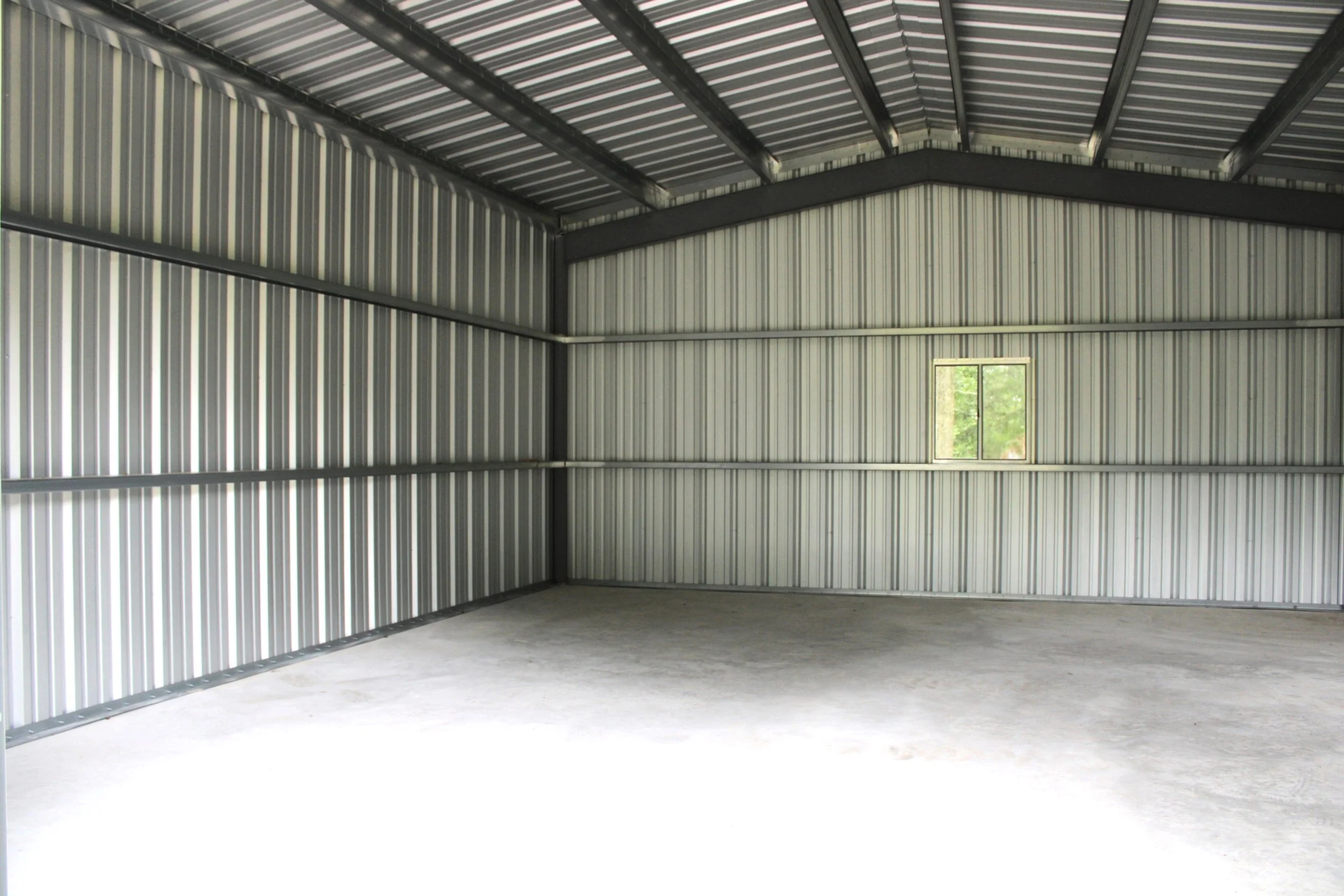 Interior view showing the weld-up steel framing, galvanized roof and wall purlins, metal wall panels, concrete slab and window.