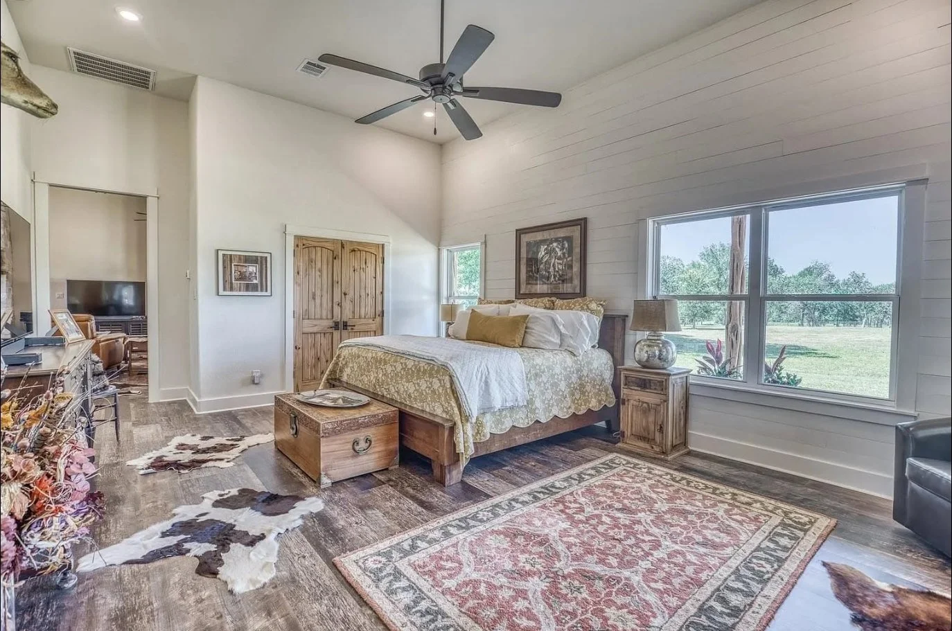 Spacious primary bedroom featuring vaulted ceilings, a shiplap accent wall, custom wood doors, large windows, and rustic finishes.
