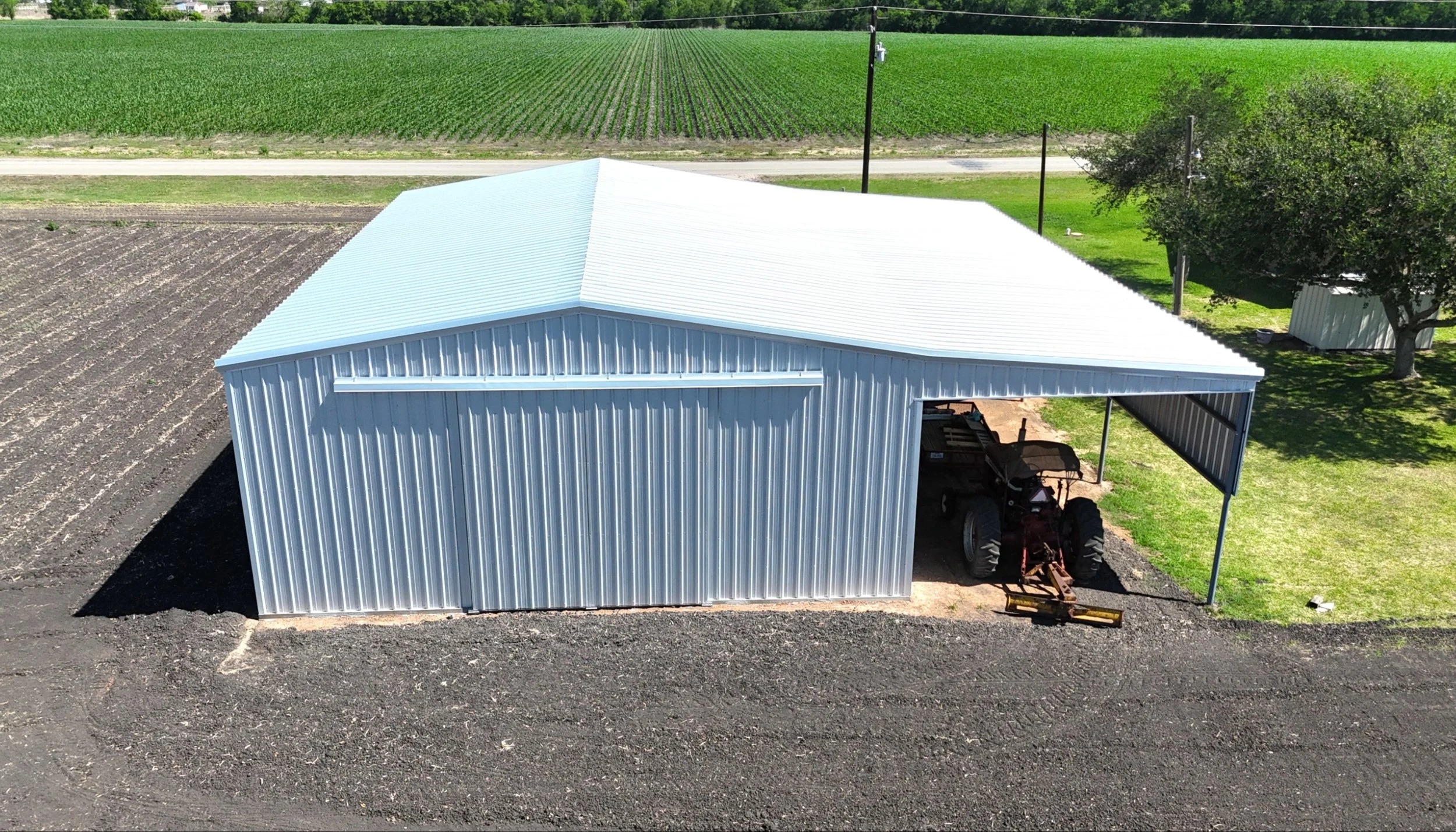 Agricultural shop with galvalume metal siding and roof, East Bernard TX, rear aerial view showing full structure and surrounding farmland