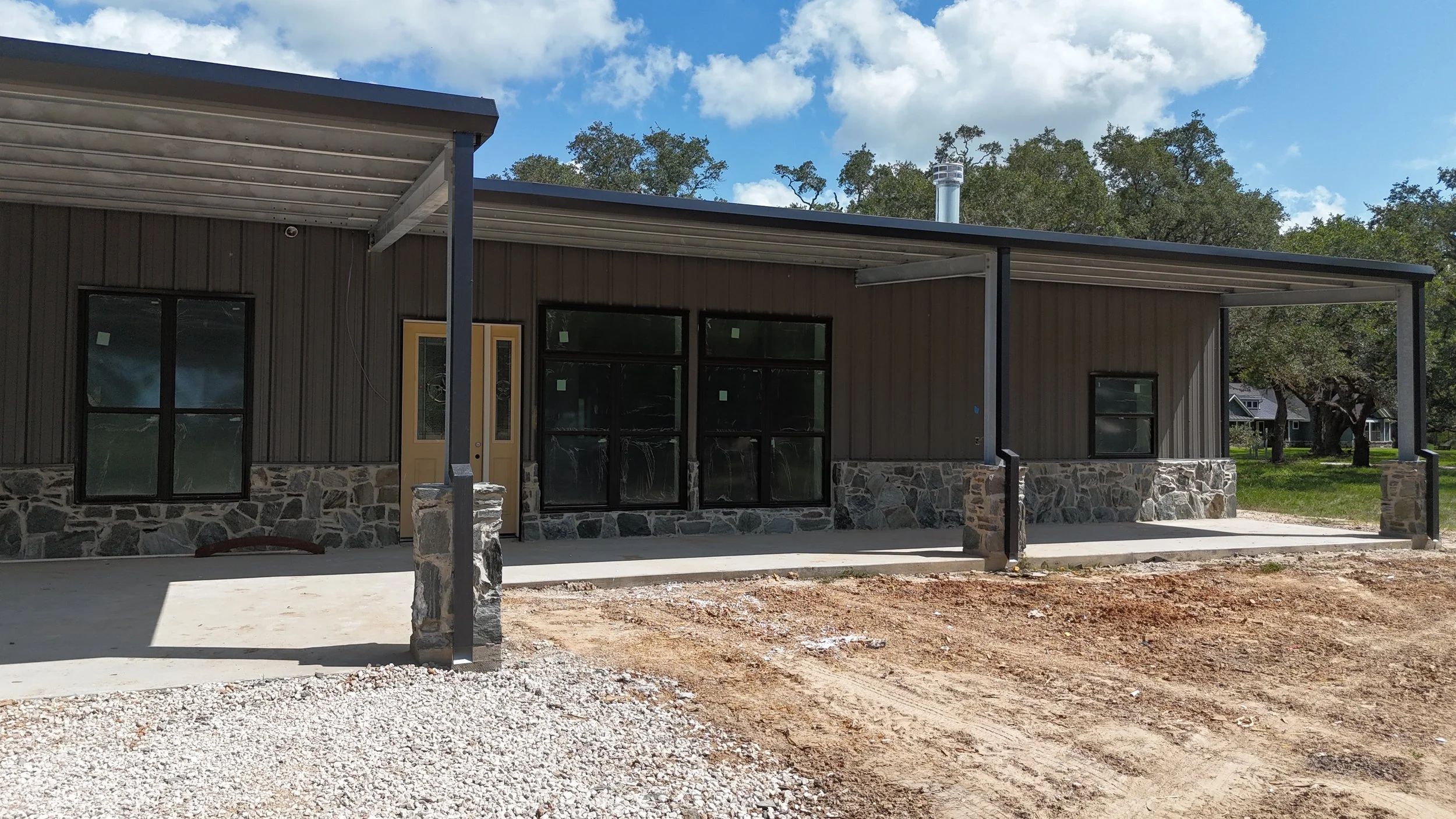 Covered front porch featuring black-framed windows, Charcoal Gray metal siding, black trim, and custom stone wainscoting.