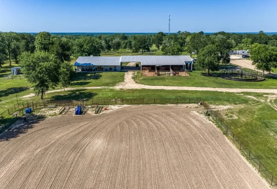 Aerial view showing the custom barndominium, four-stall horse barn, covered breezeway, paddocks, horse walker, and roping arena.