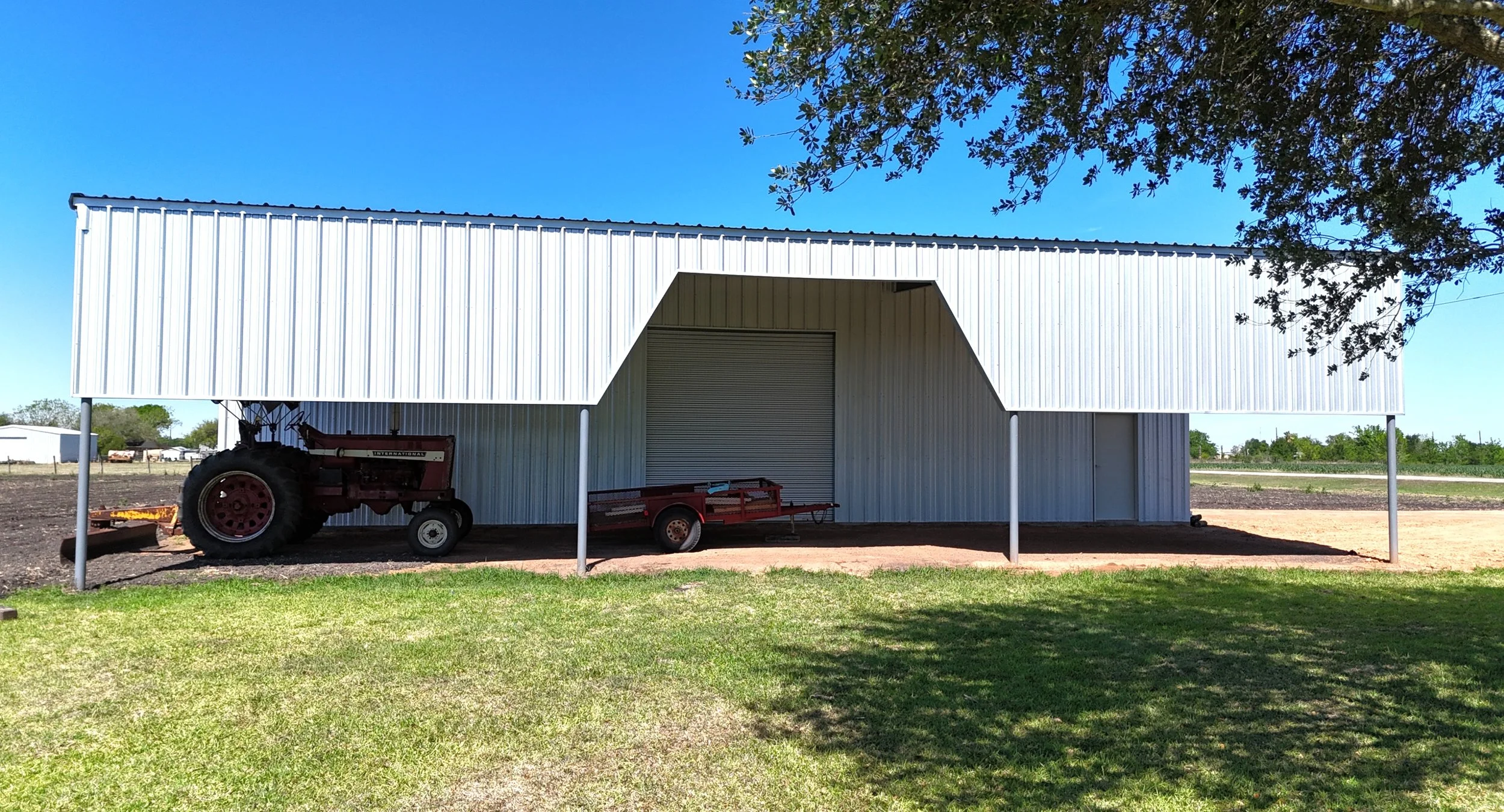 Agricultural shop with large roll-up door and covered side parking, galvalume metal building, East Bernard TX