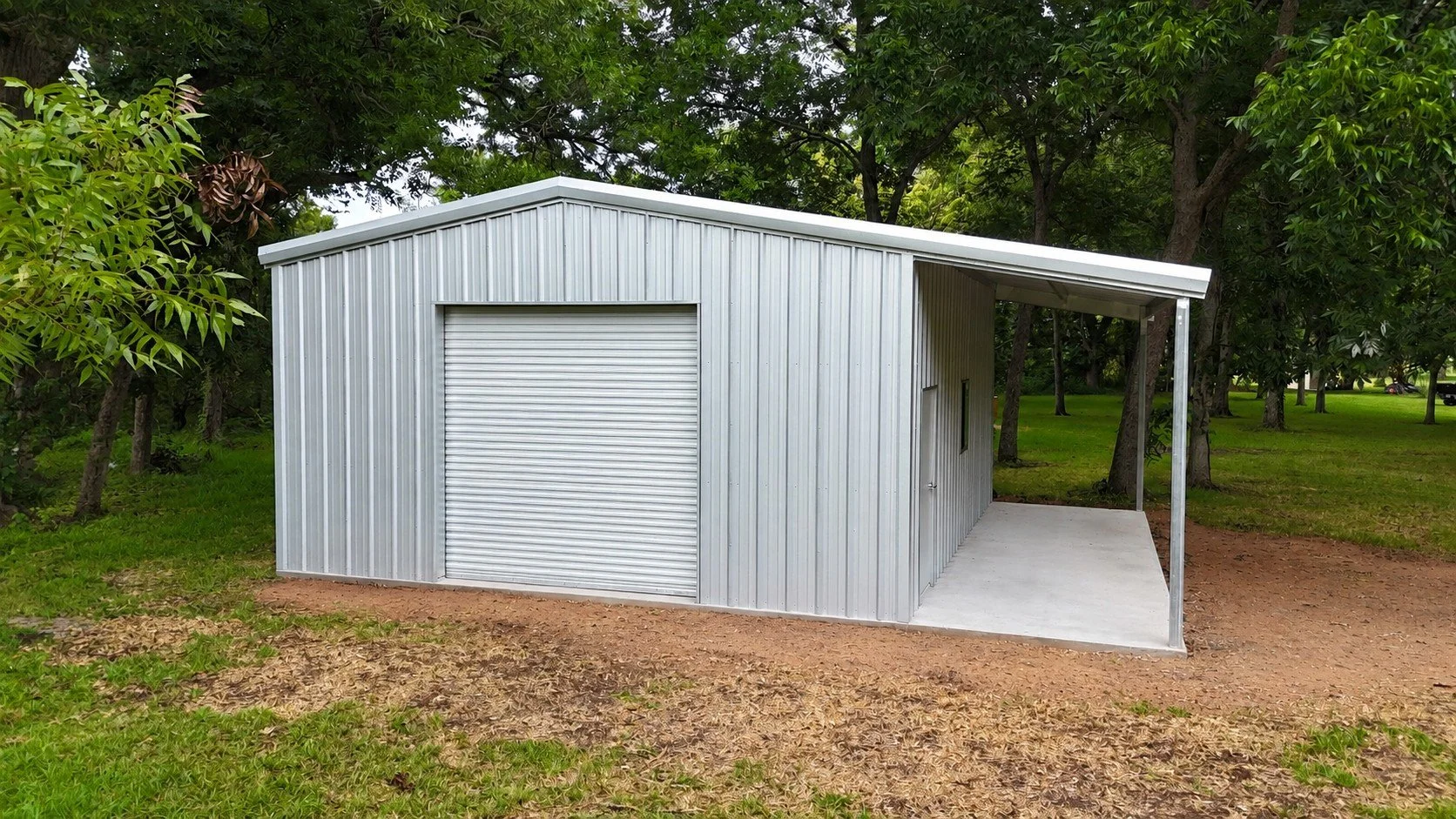 Front view of the custom 28' x 24' weld-up metal building in Bailey’s Prairie, Texas, featuring a white roll-up door, walk door, window, and full-length side lean-to.