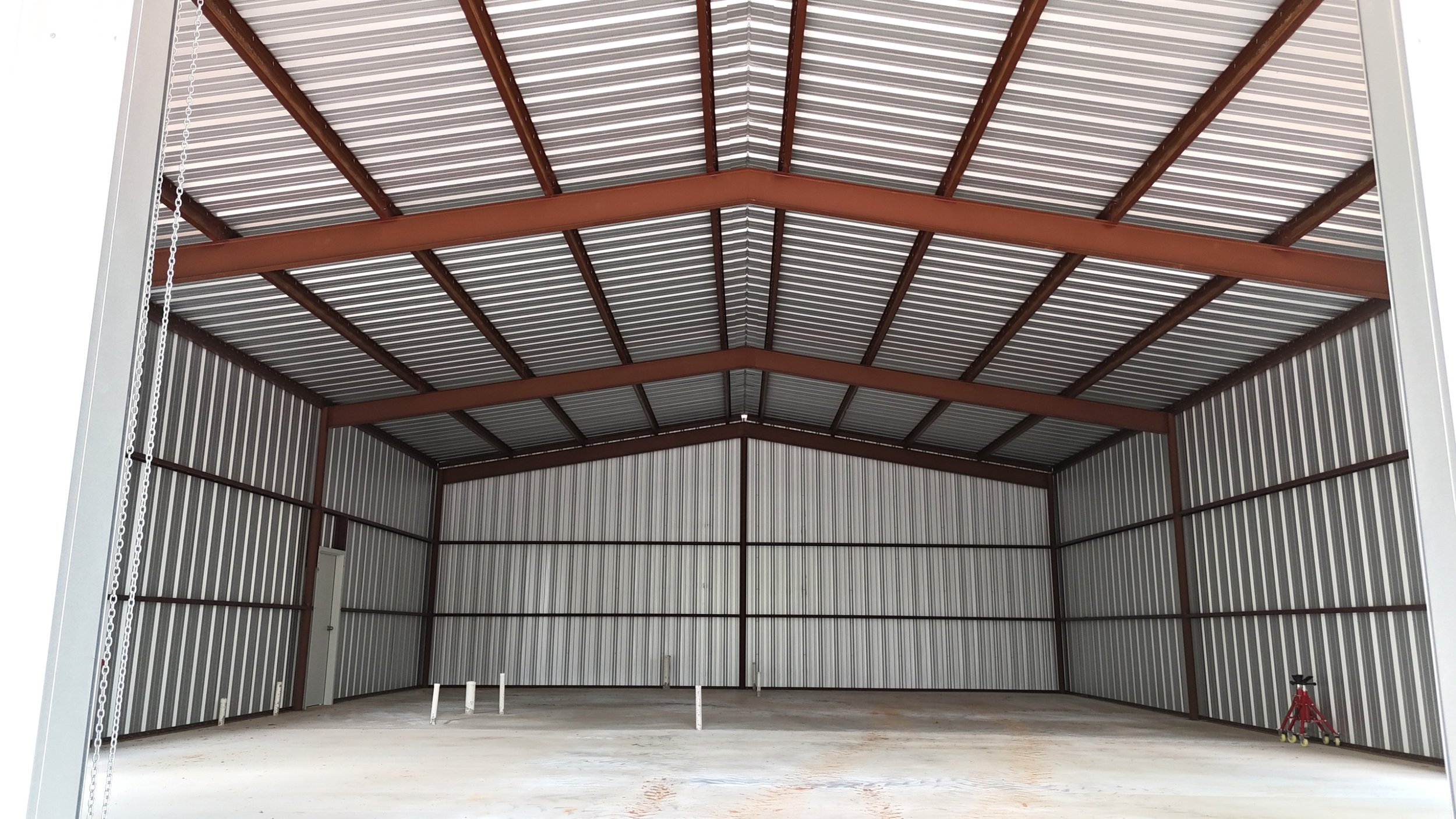 Interior view of welded metal shop showing open span workspace, Galvalume walls, concrete slab, and high-clearance roof structure