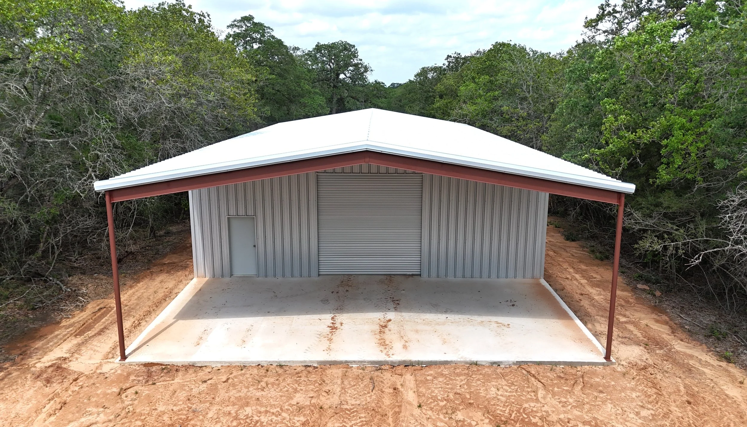 Front angle view of metal building with large covered awning, roll-up shop door, and reinforced concrete slab in Gonzales County, TX