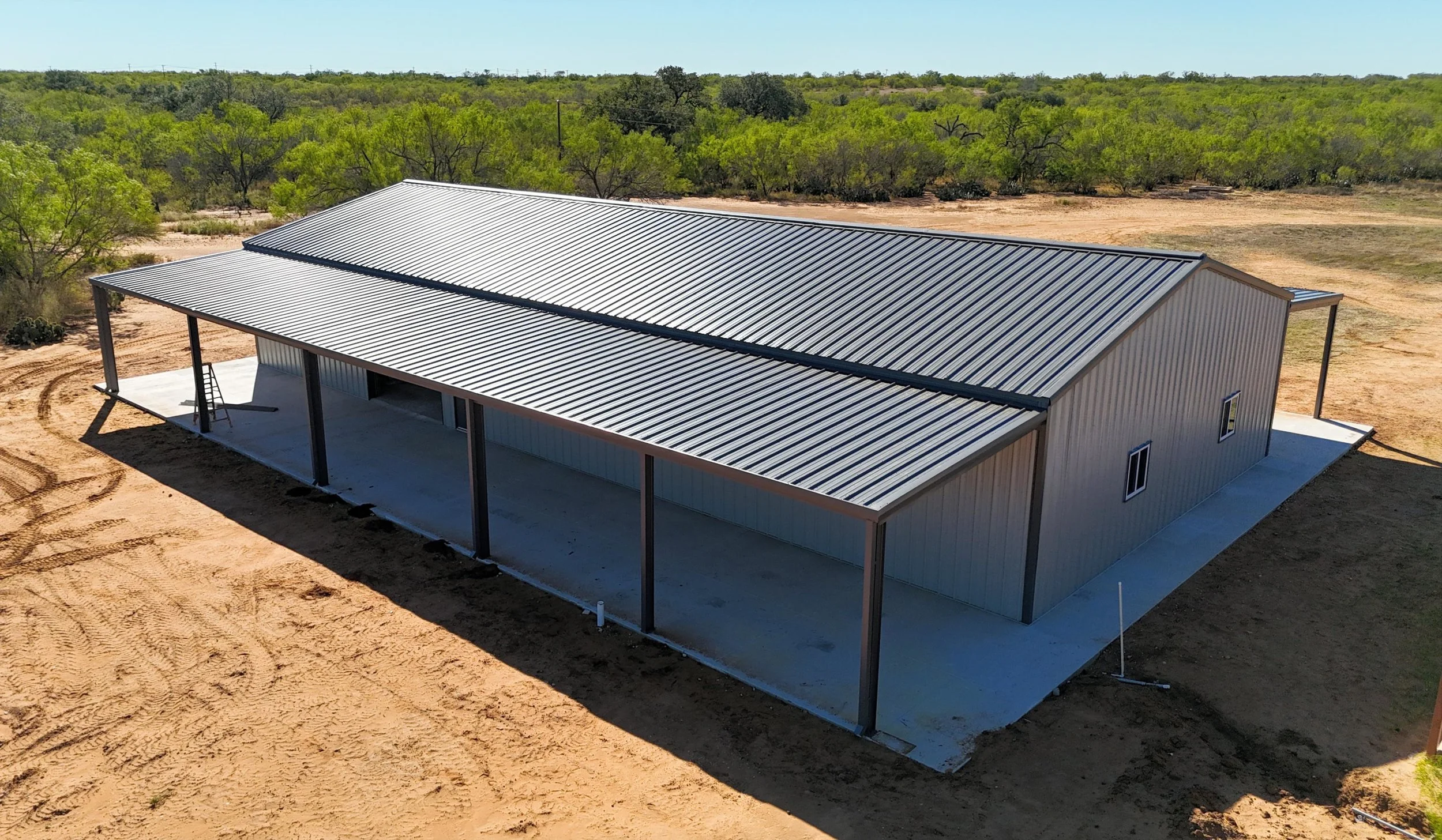 Backside view of insulated Mueller metal building barndominium in Bigfoot Texas with dark charcoal roof and lean-to overhang.