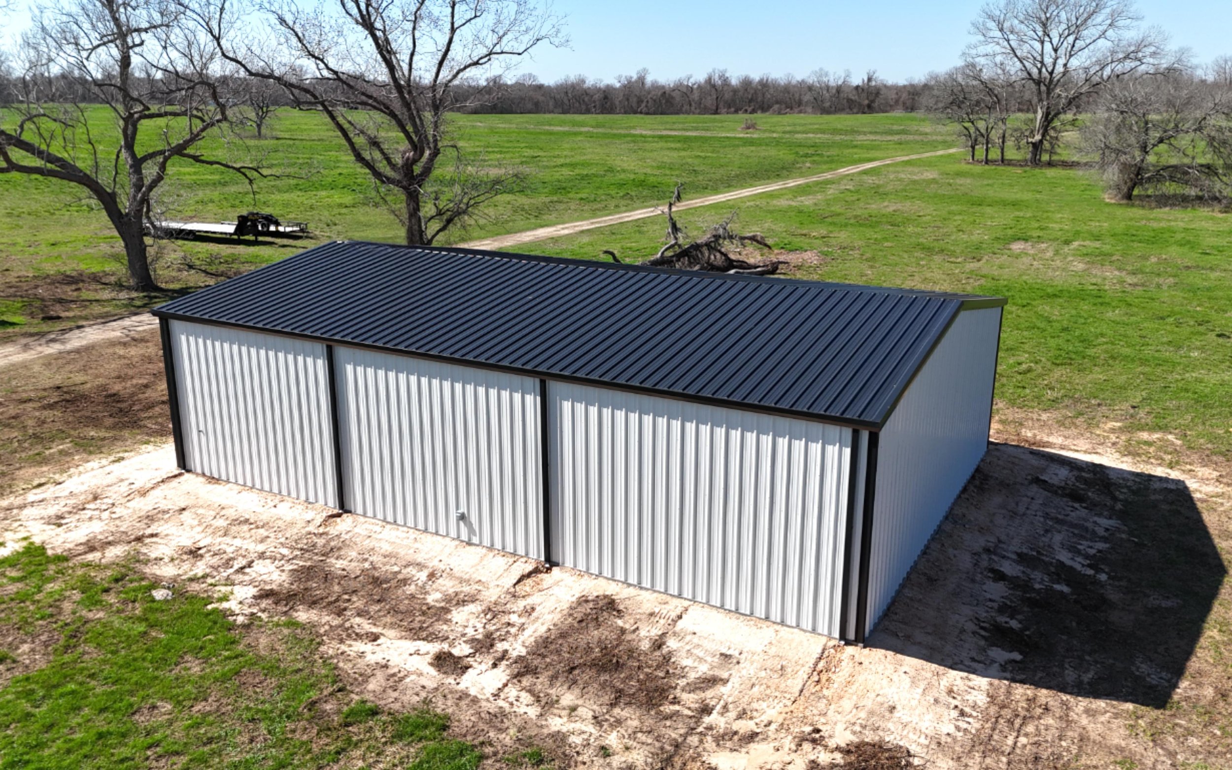 Side profile of 40x60 custom metal building in Fort Bend County with black roof, white wall panels, and installed gutters and downspouts for long-term slab protection.