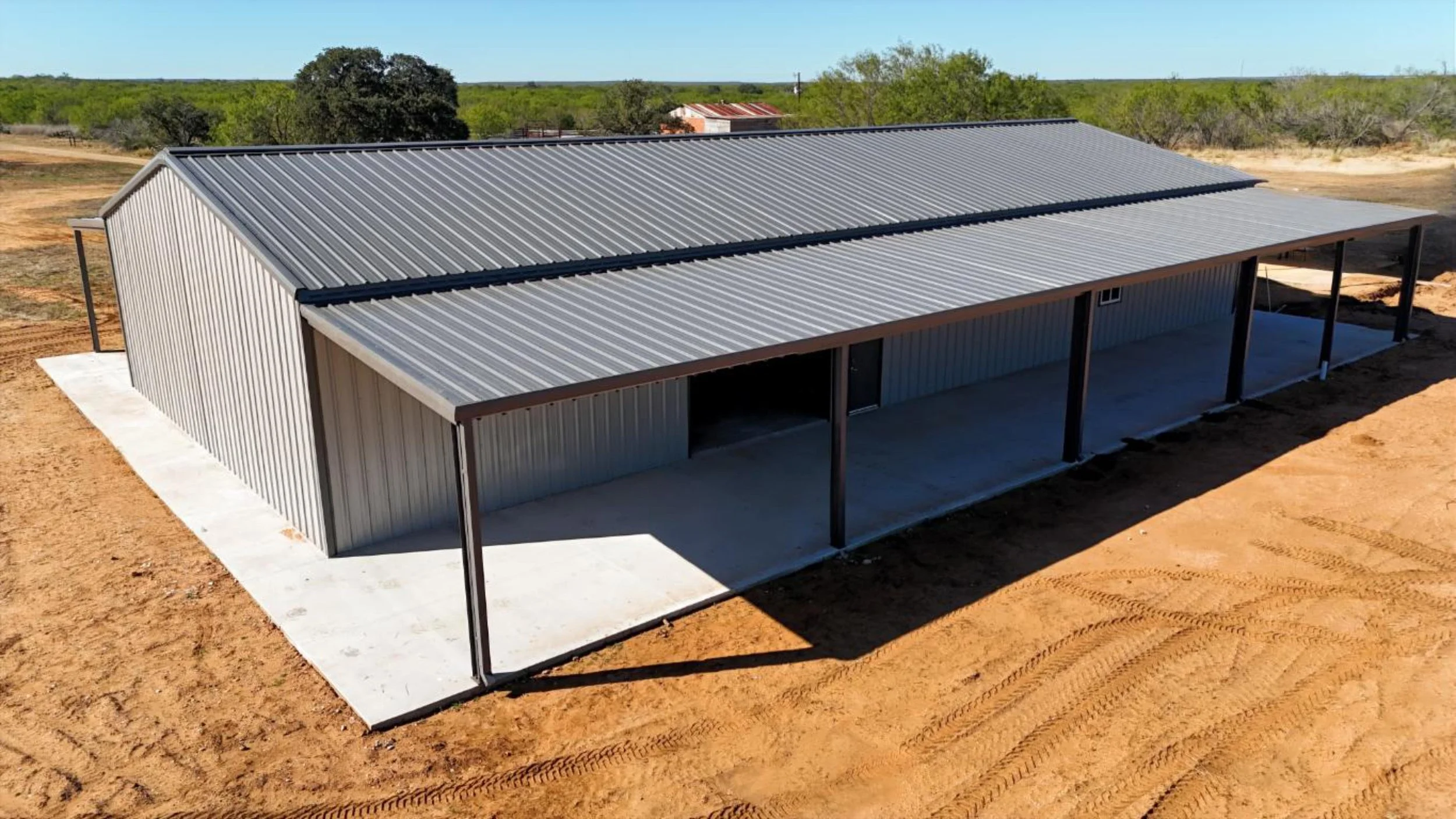 Large Mueller metal barndominium in Bigfoot Texas with charcoal roof and dual lean-to covered porches on concrete slab