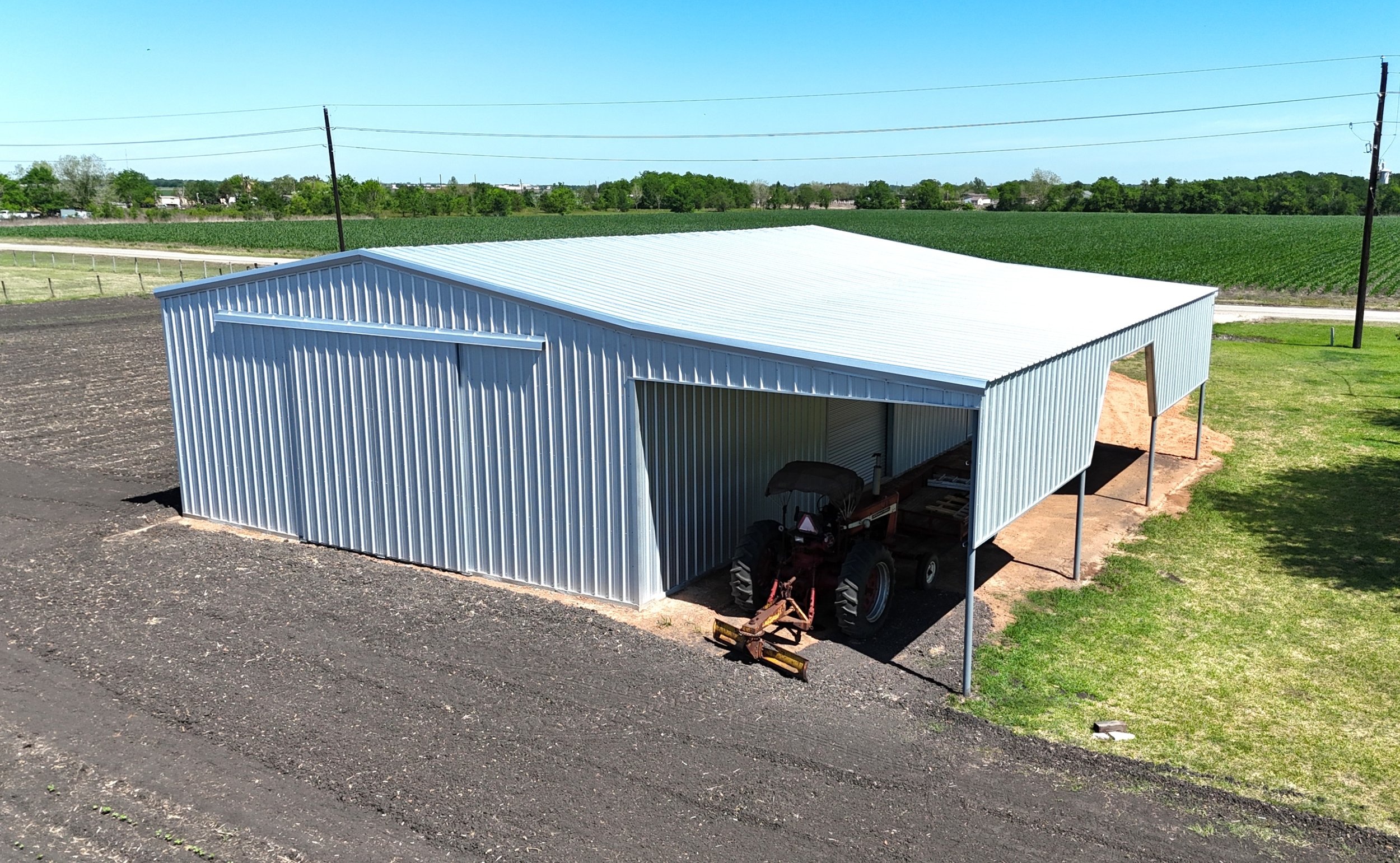 Galvalume agricultural shop with lean-to cover and tractor underneath, East Bernard TX, elevated rear view