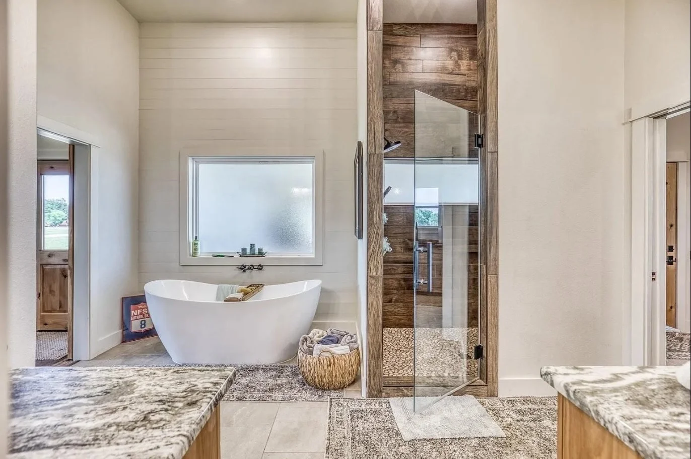 Custom primary bathroom with a freestanding soaking tub, oversized walk-in shower, wood-look tile, glass enclosure, and dual vanities.