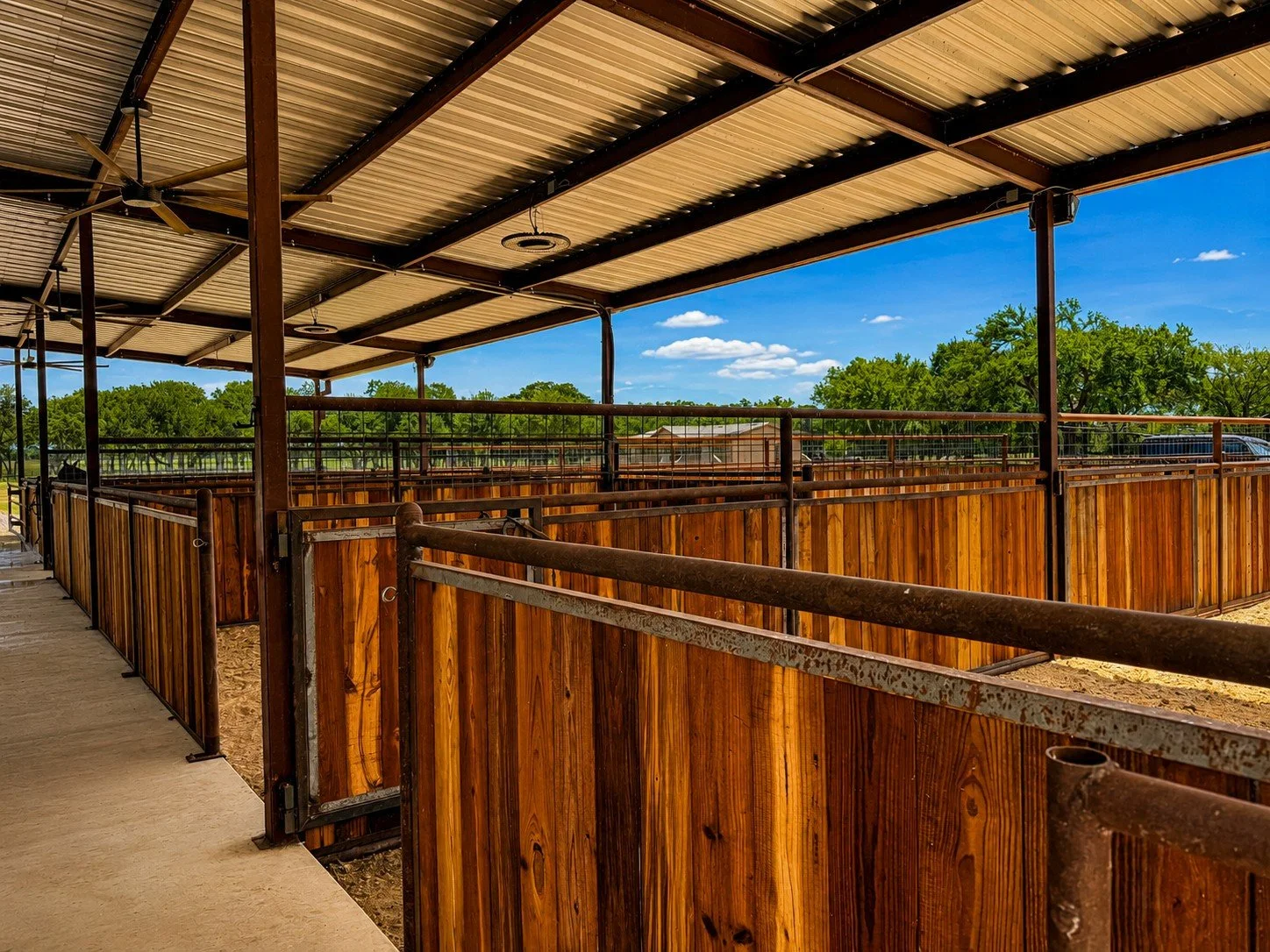 Custom welded horse stalls with creosote wood boards under a covered steel barn in Caldwell, Texas.