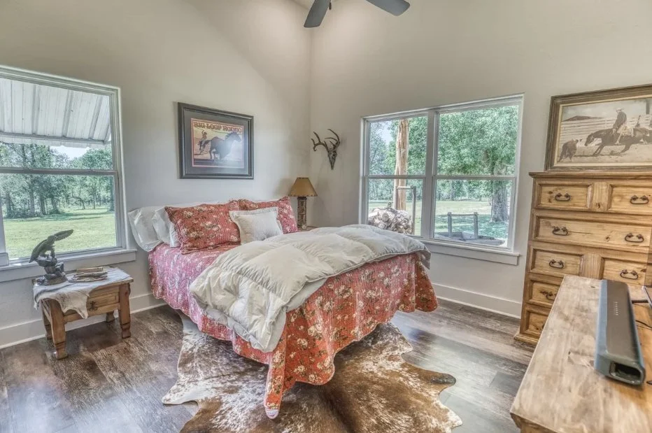 Bright secondary bedroom with vaulted ceilings, large windows, wood-look flooring, and views of the surrounding Washington County property.