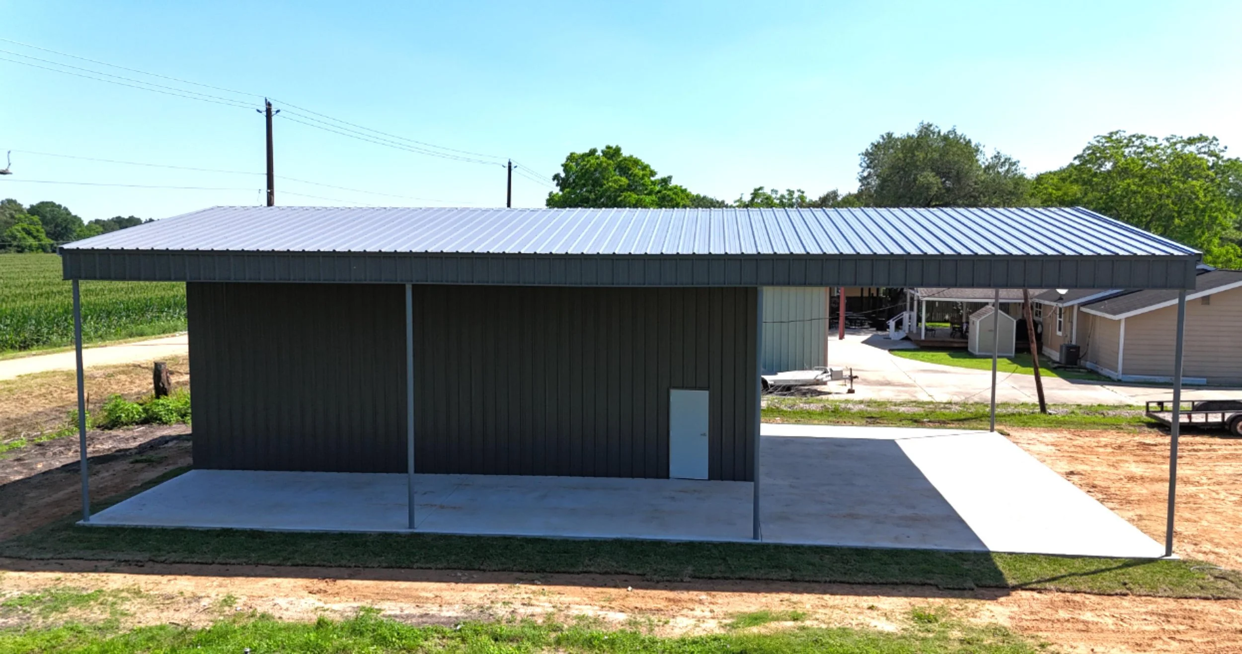 Side view of custom metal building in Richmond TX featuring large covered awning, walk door, and charcoal grey siding