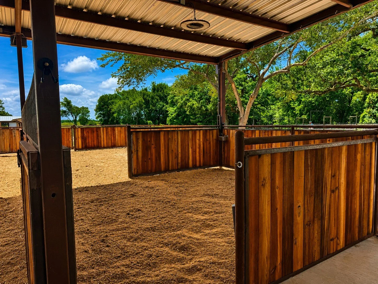 Covered horse stall aisle featuring custom welded steel stalls with creosote wood boards in Caldwell, Texas.