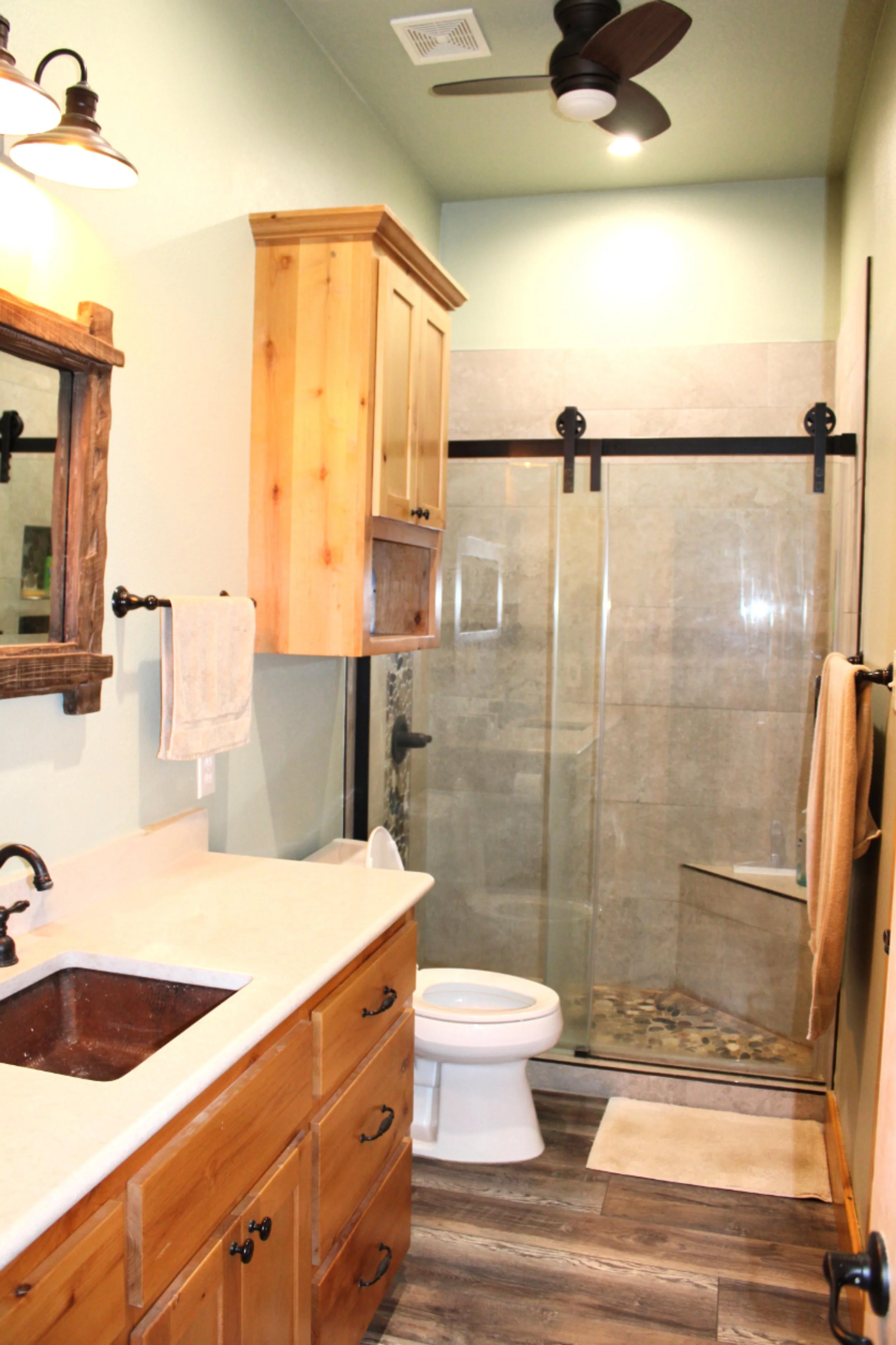 Custom bathroom inside barndominium featuring walk-in shower with sliding glass barn door hardware and rustic cabinetry.