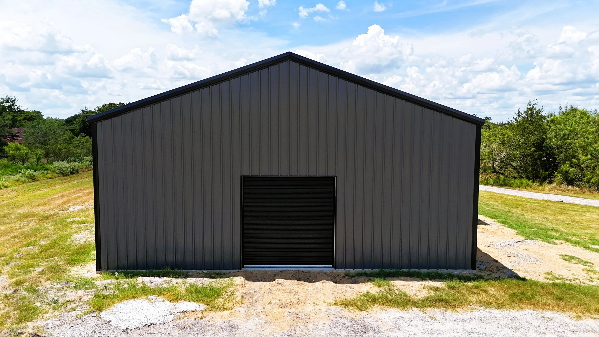 End view of a custom metal shop/home combination highlighting the large insulated roll-up door, weld-up steel construction, and durable charcoal gray exterior.